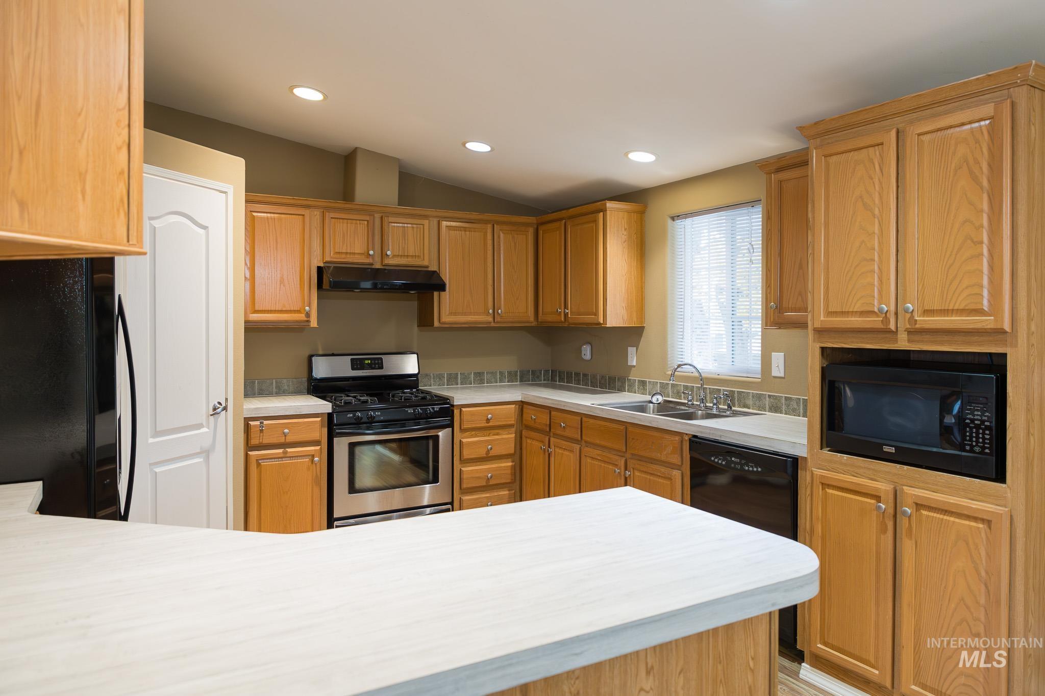 Kitchen featuring black appliances, light countertops, recessed lighting, vaulted ceiling, and under cabinet range hood
