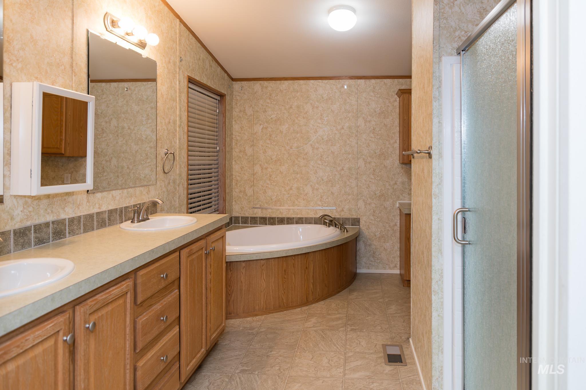 Bathroom with double vanity, wallpapered walls, a garden tub, crown molding, and a stall shower