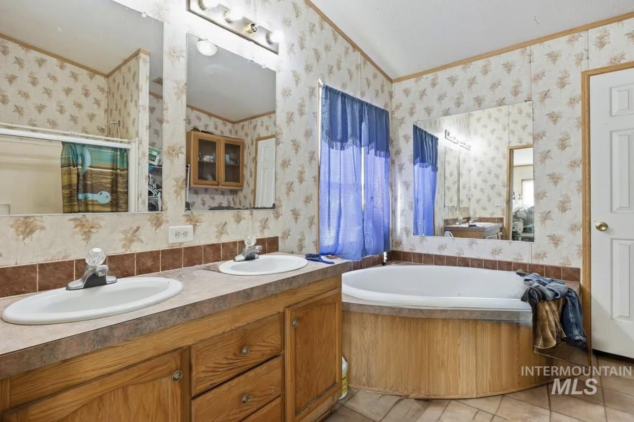 Bathroom with double vanity, a bath, crown molding, light tile patterned floors, and wallpapered walls