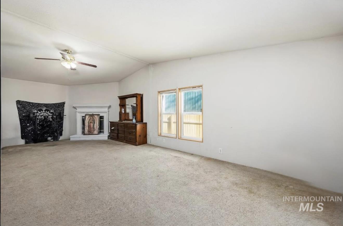 Unfurnished living room featuring light colored carpet, vaulted ceiling, and a ceiling fan