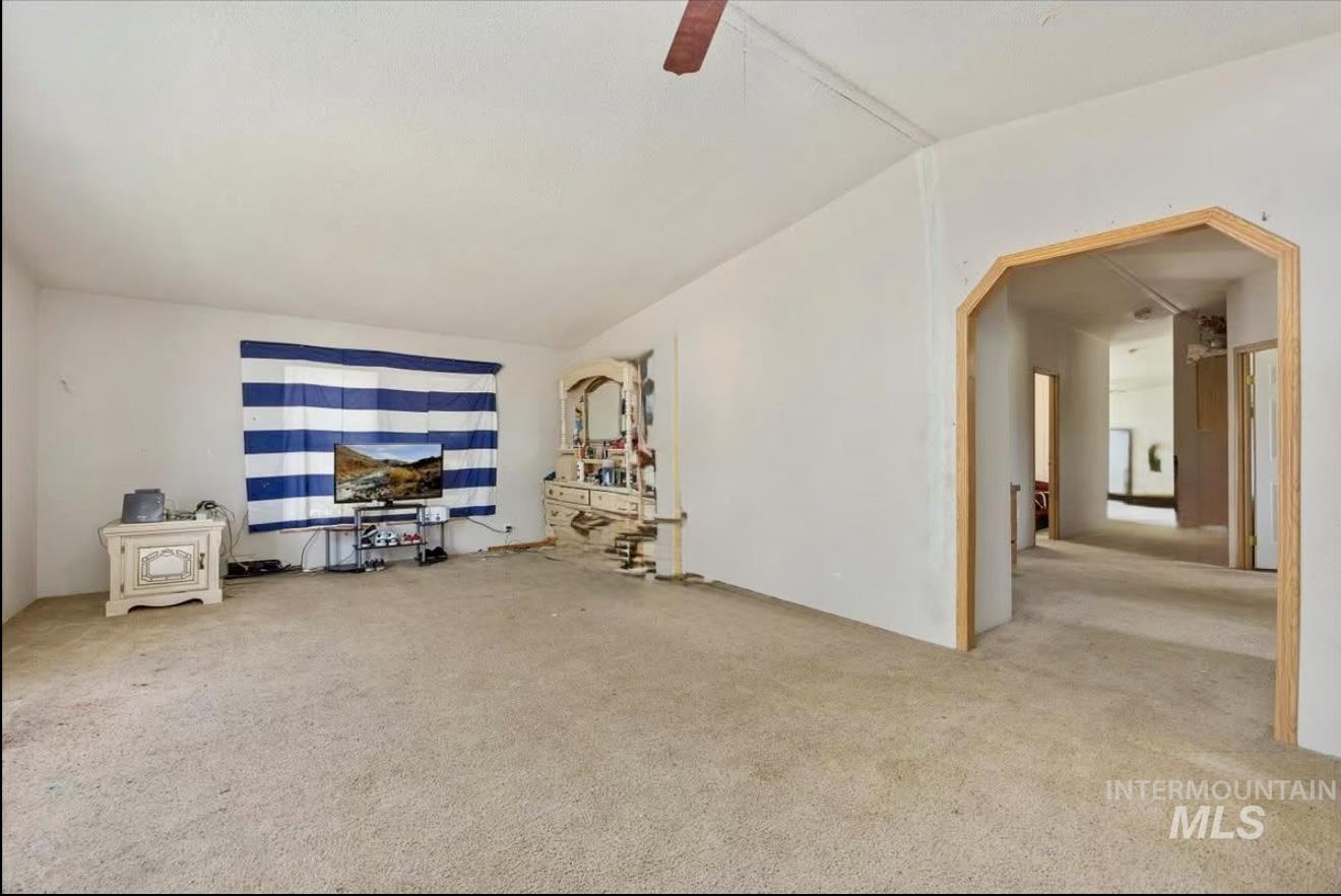 Unfurnished living room featuring carpet floors, arched walkways, vaulted ceiling, and a ceiling fan