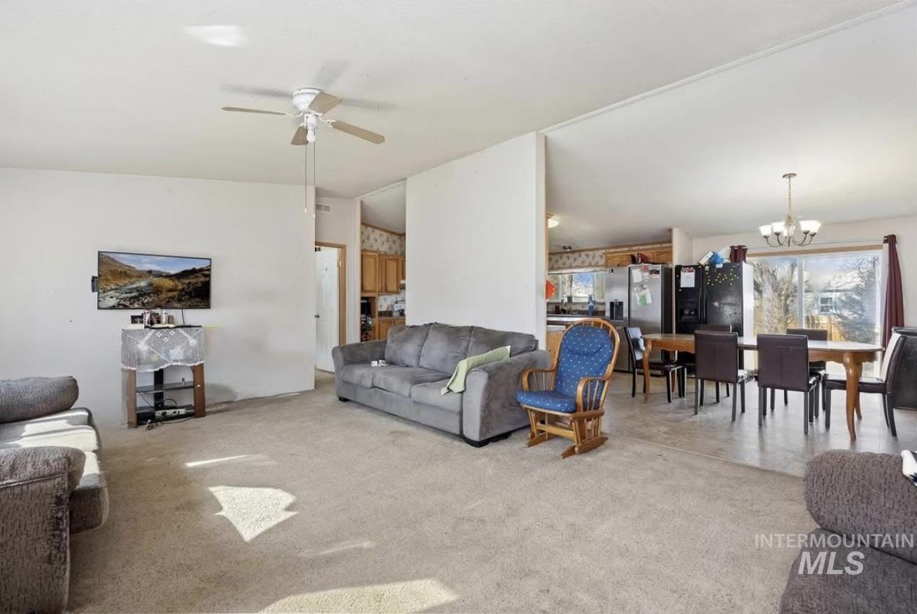 Carpeted living area featuring lofted ceiling, a chandelier, and ceiling fan