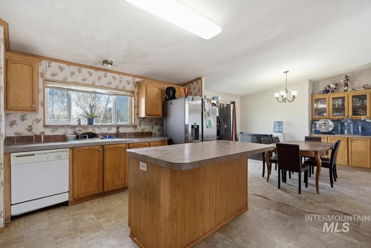 Kitchen featuring a center island, backsplash, white dishwasher, a chandelier, and pendant lighting