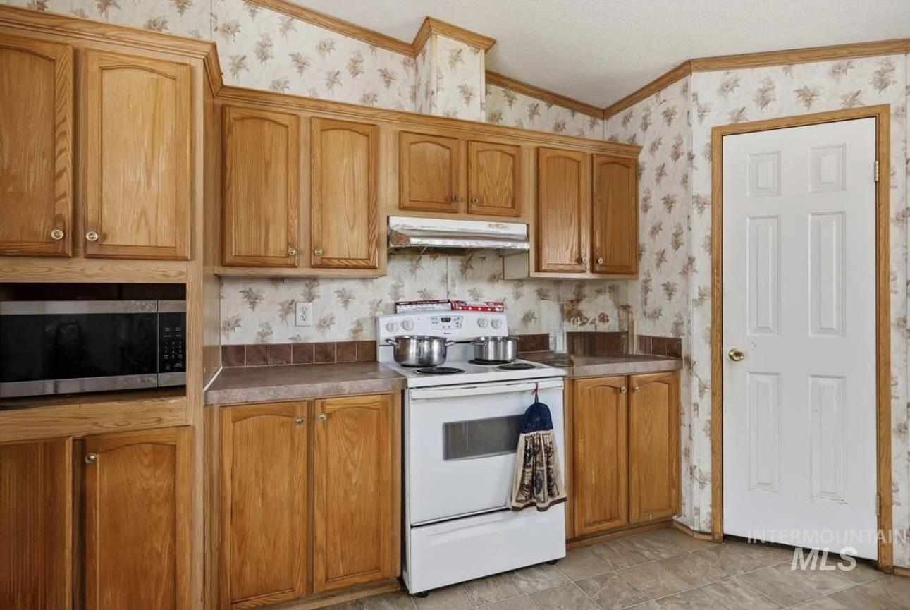 Kitchen with wallpapered walls, white electric range oven, stainless steel microwave, under cabinet range hood, and crown molding