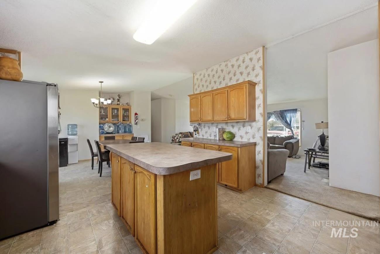 Kitchen with freestanding refrigerator, a kitchen island, a chandelier, decorative light fixtures, and brown cabinets