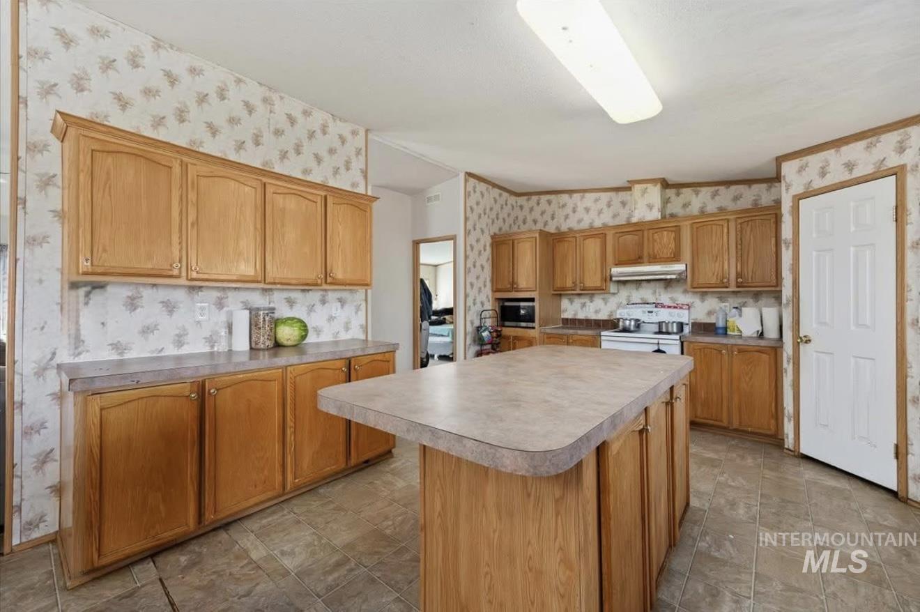 Kitchen with a kitchen island, wallpapered walls, white stove, light countertops, and under cabinet range hood