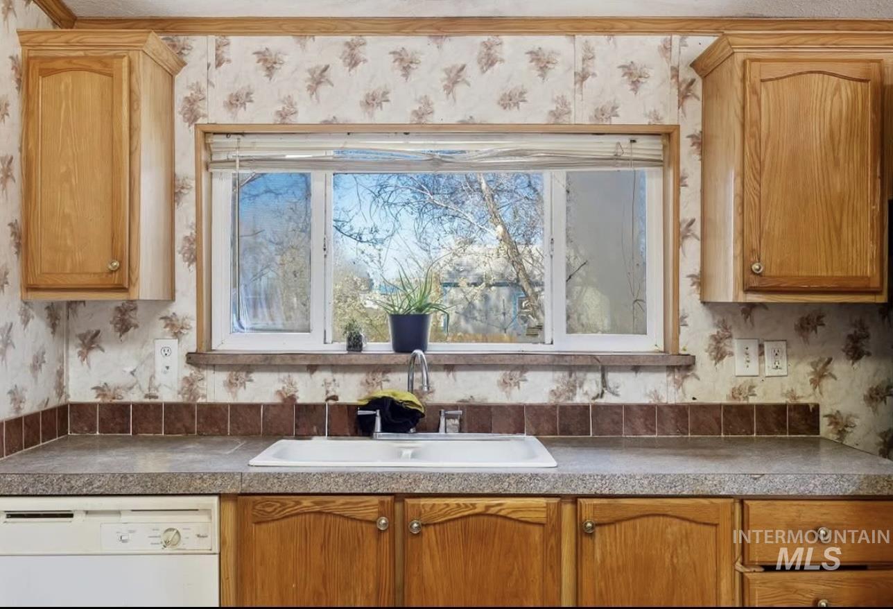 Kitchen featuring wallpapered walls, dishwasher, brown cabinets, and light countertops