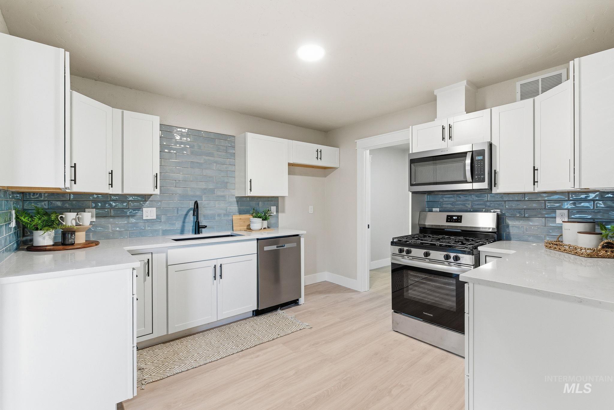 Kitchen featuring appliances with stainless steel finishes, tasteful backsplash, light stone countertops, and white cabinetry