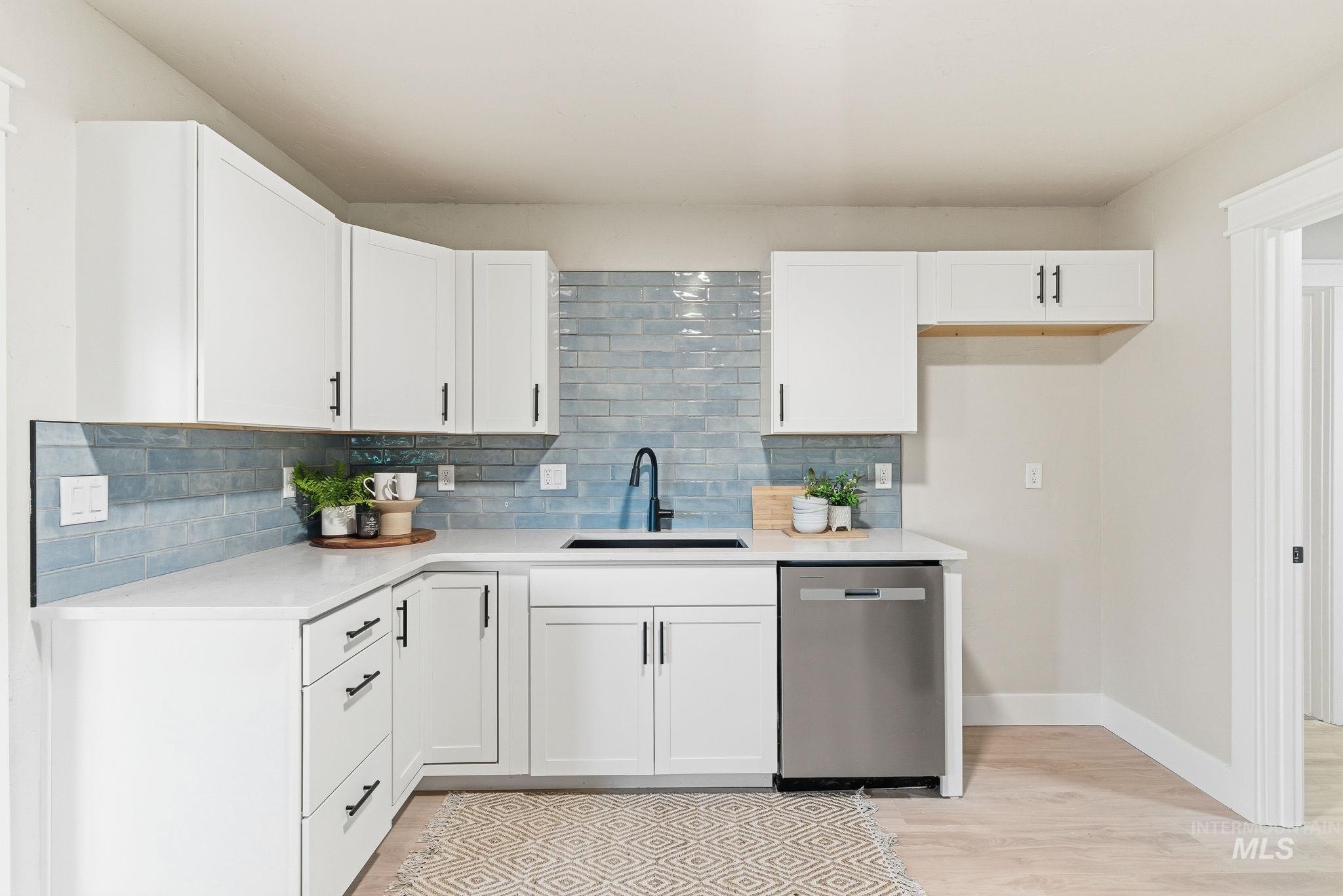 Kitchen with white cabinets, dishwasher, light wood-style floors, backsplash, and light stone countertops