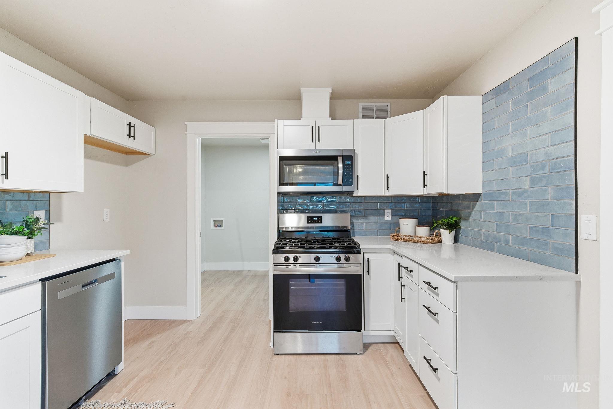Kitchen featuring decorative backsplash, appliances with stainless steel finishes, white cabinetry, and light wood-style flooring