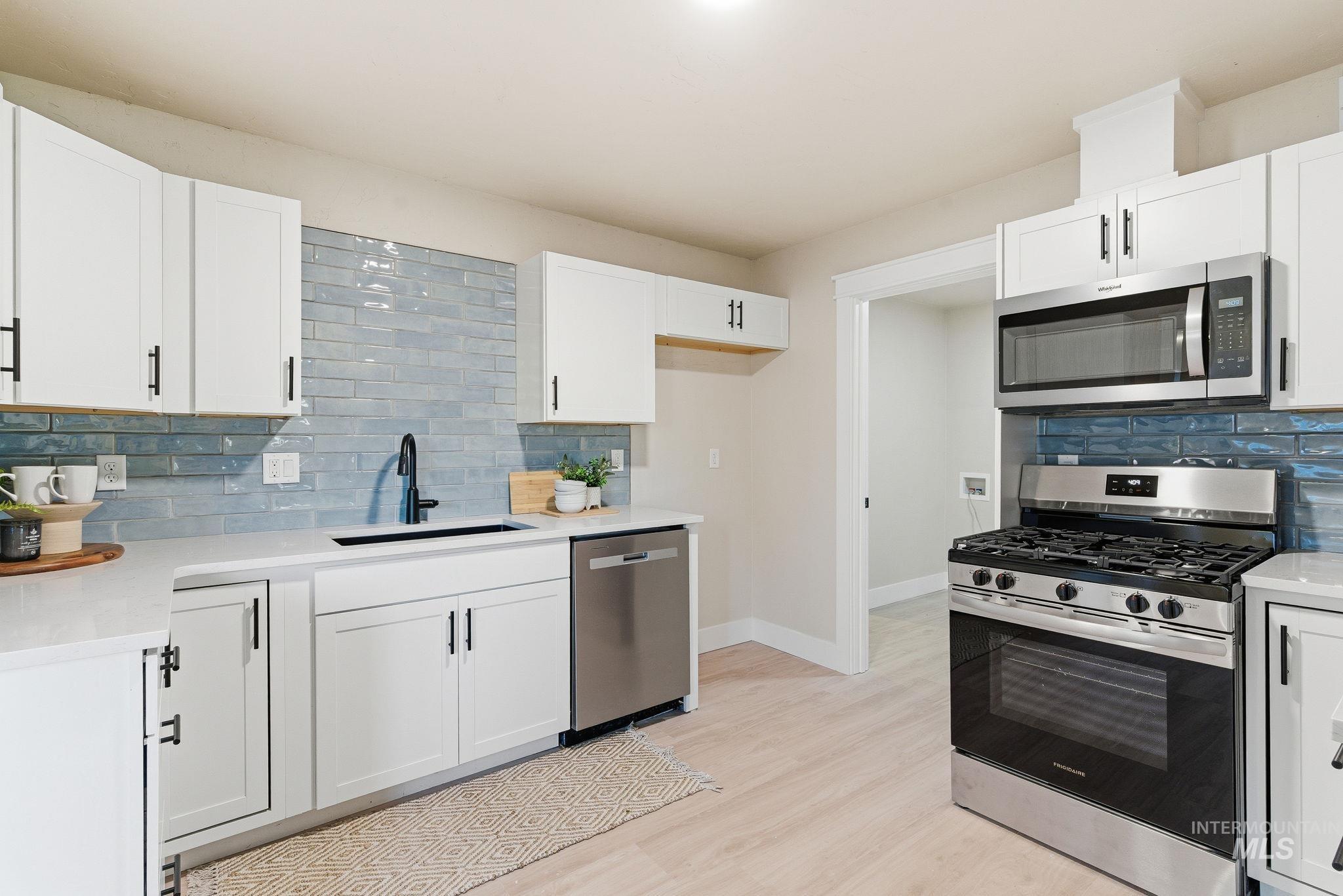Kitchen featuring tasteful backsplash, stainless steel appliances, white cabinetry, and light wood-type flooring