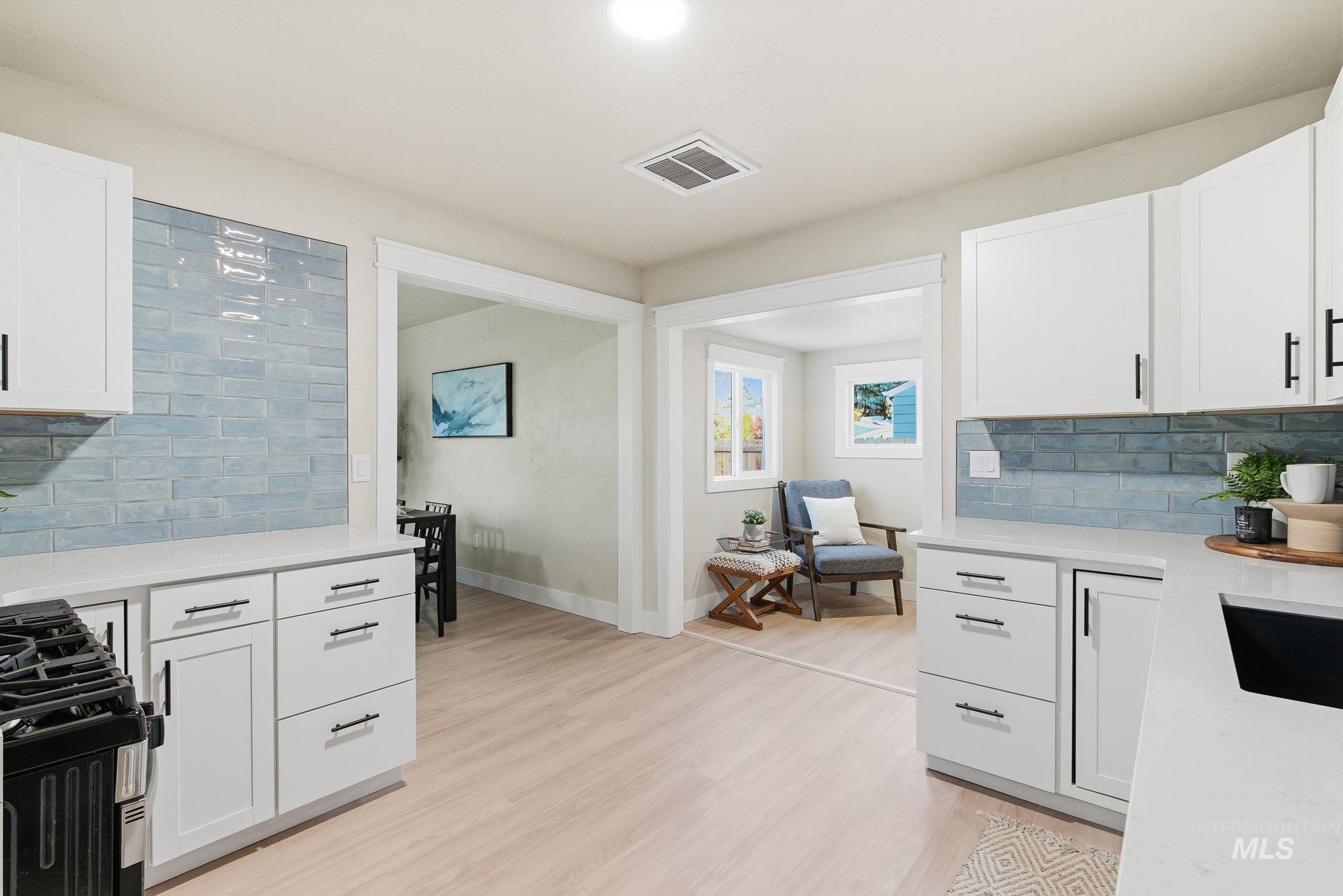 Kitchen with tasteful backsplash, white cabinetry, gas stove, light wood-style flooring, and light stone counters