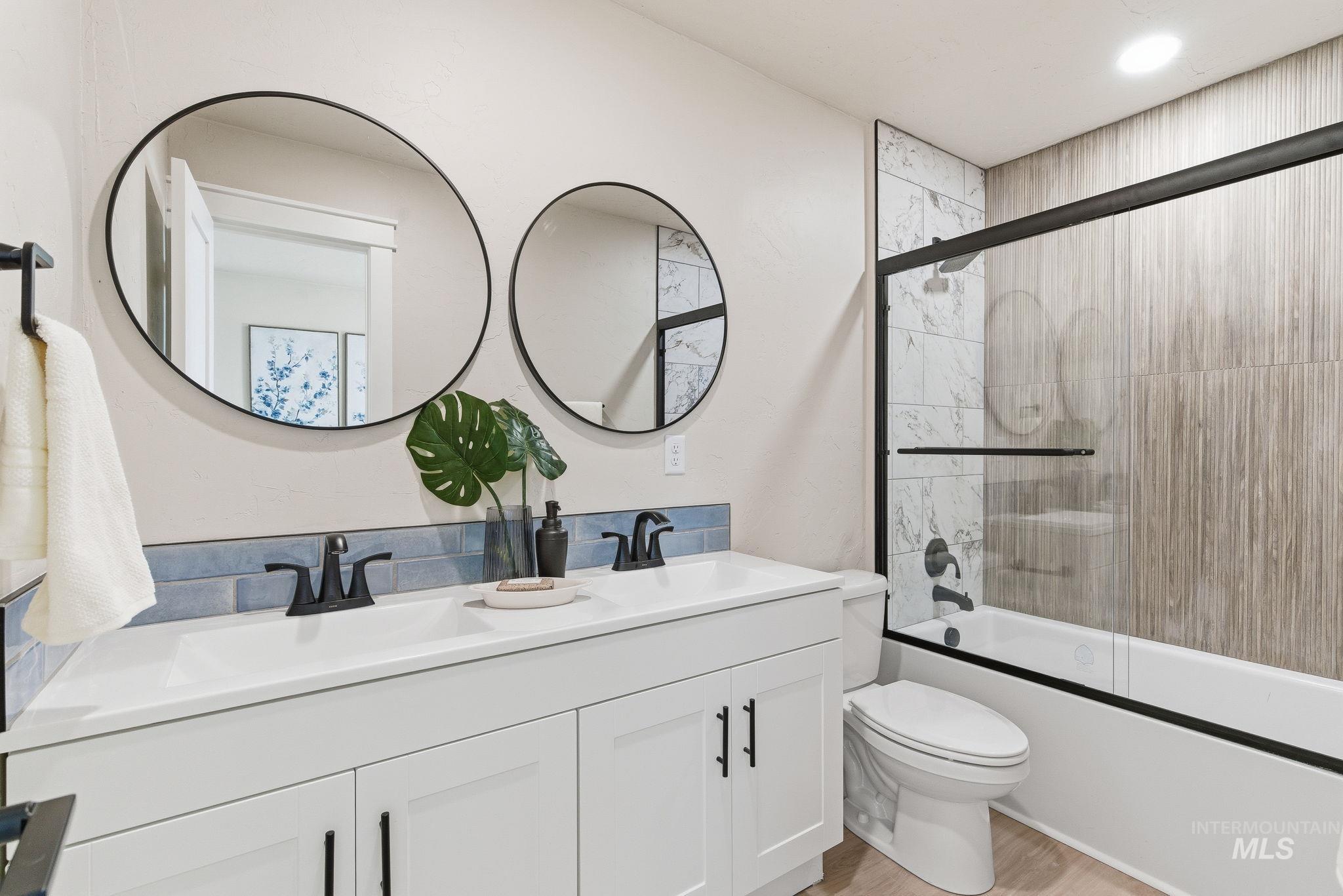 Bathroom featuring double vanity, enclosed tub / shower combo, and light wood-type flooring