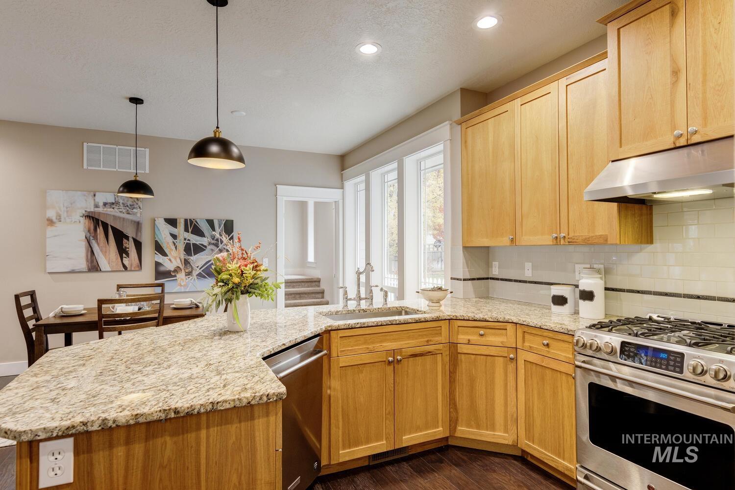 Kitchen with appliances with stainless steel finishes, under cabinet range hood, hanging light fixtures, light stone counters, and recessed lighting