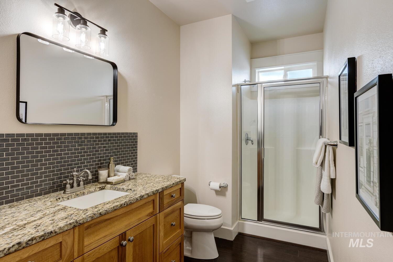 Bathroom featuring vanity, a stall shower, dark wood-style floors, and decorative backsplash