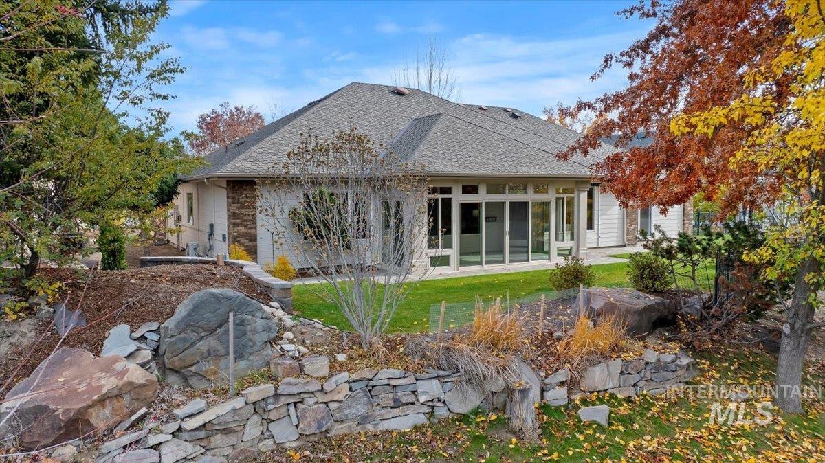 Back of property with a sunroom, a shingled roof, and a lawn