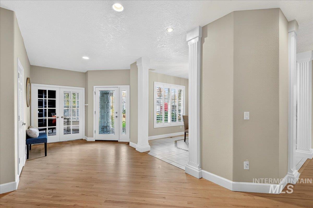 Entrance foyer with ornate columns, recessed lighting, light wood-type flooring, a textured ceiling, and french doors