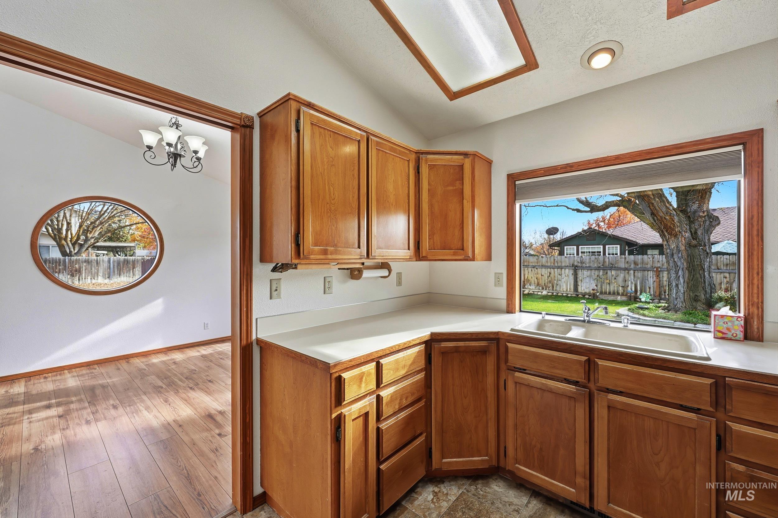 Kitchen featuring light countertops, brown cabinetry, a chandelier, vaulted ceiling, and a textured ceiling