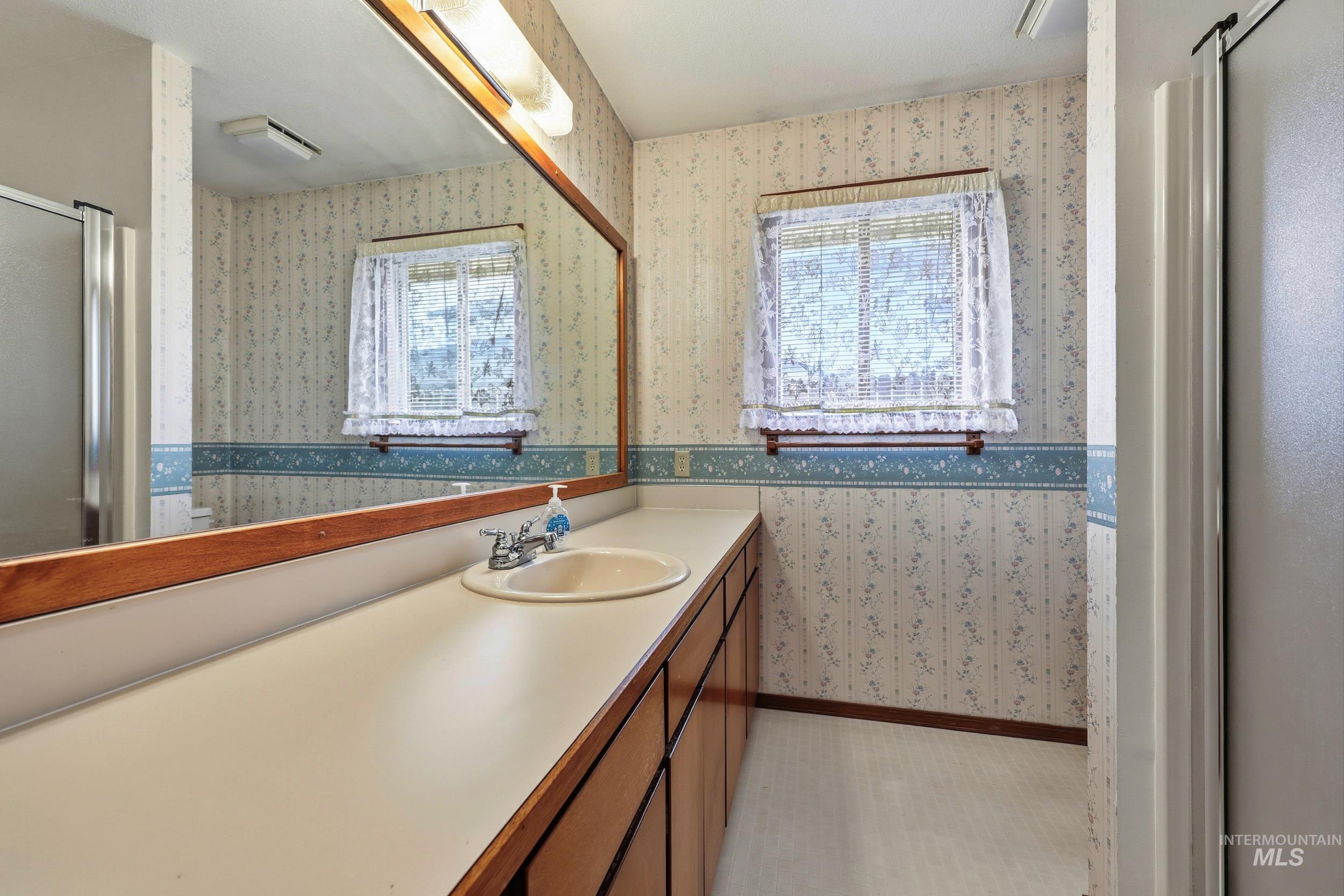 Full bathroom with wallpapered walls, vanity, and a stall shower