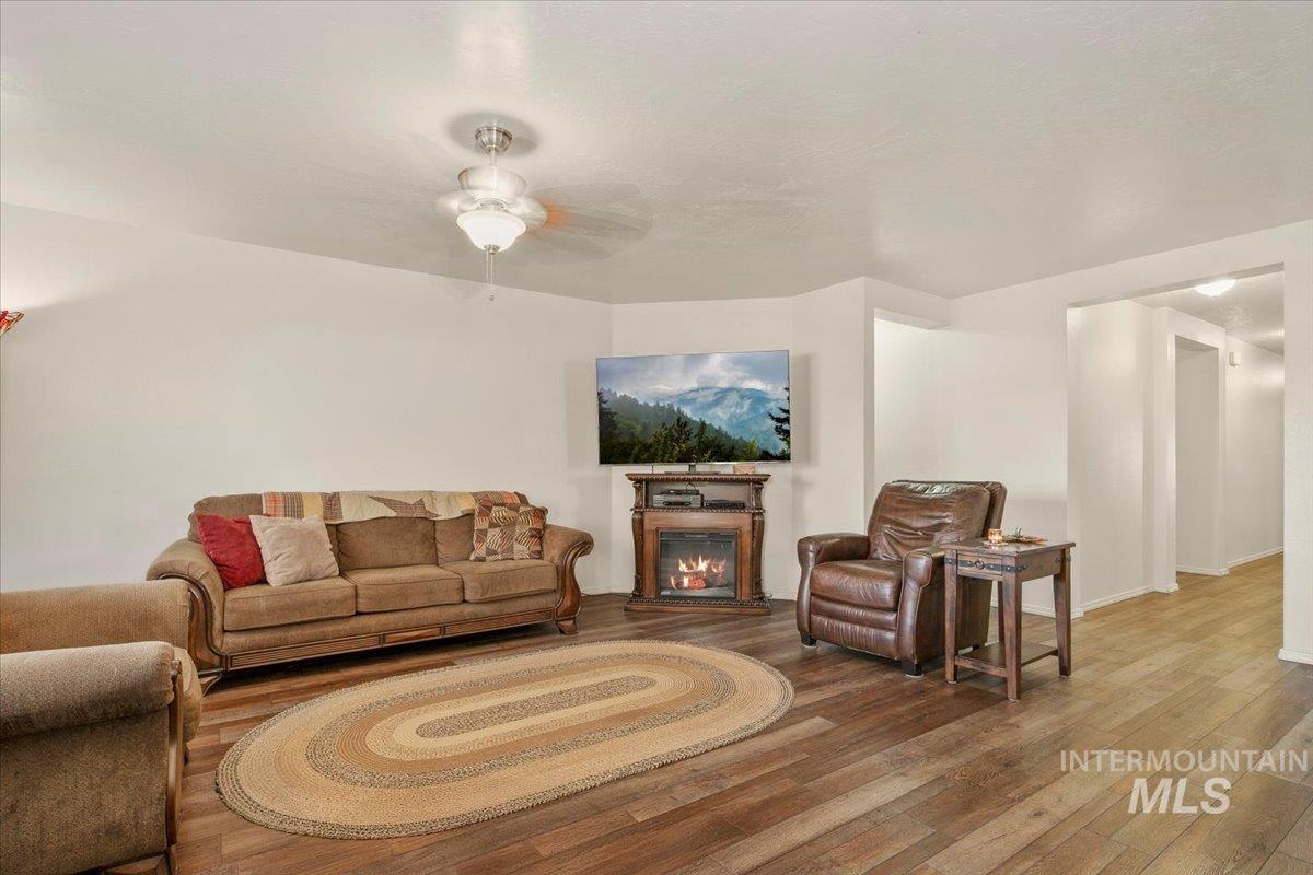 Living area with a glass covered fireplace, wood finished floors, and ceiling fan