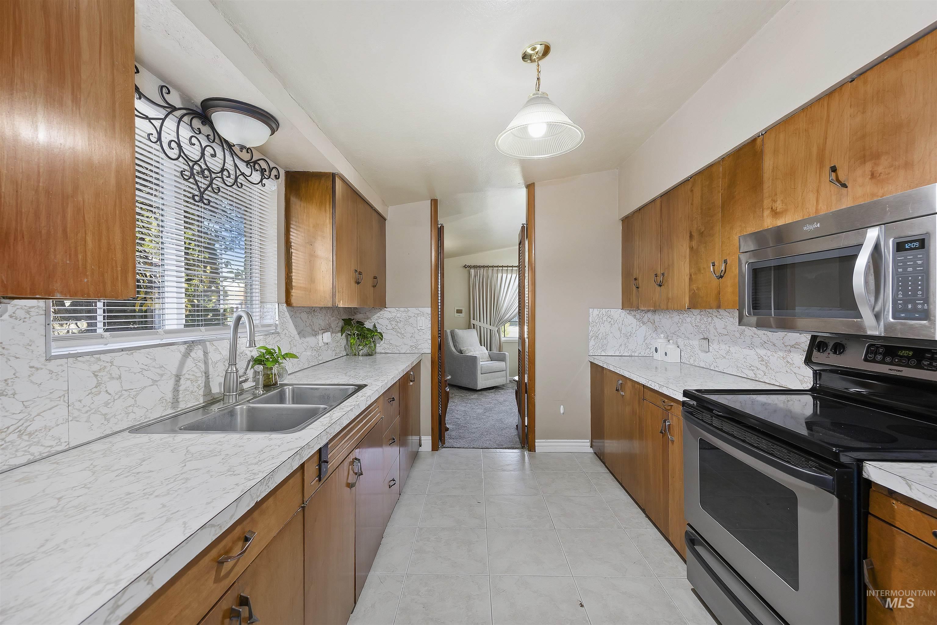 Kitchen featuring backsplash, stainless steel appliances, brown cabinets, light countertops, and pendant lighting