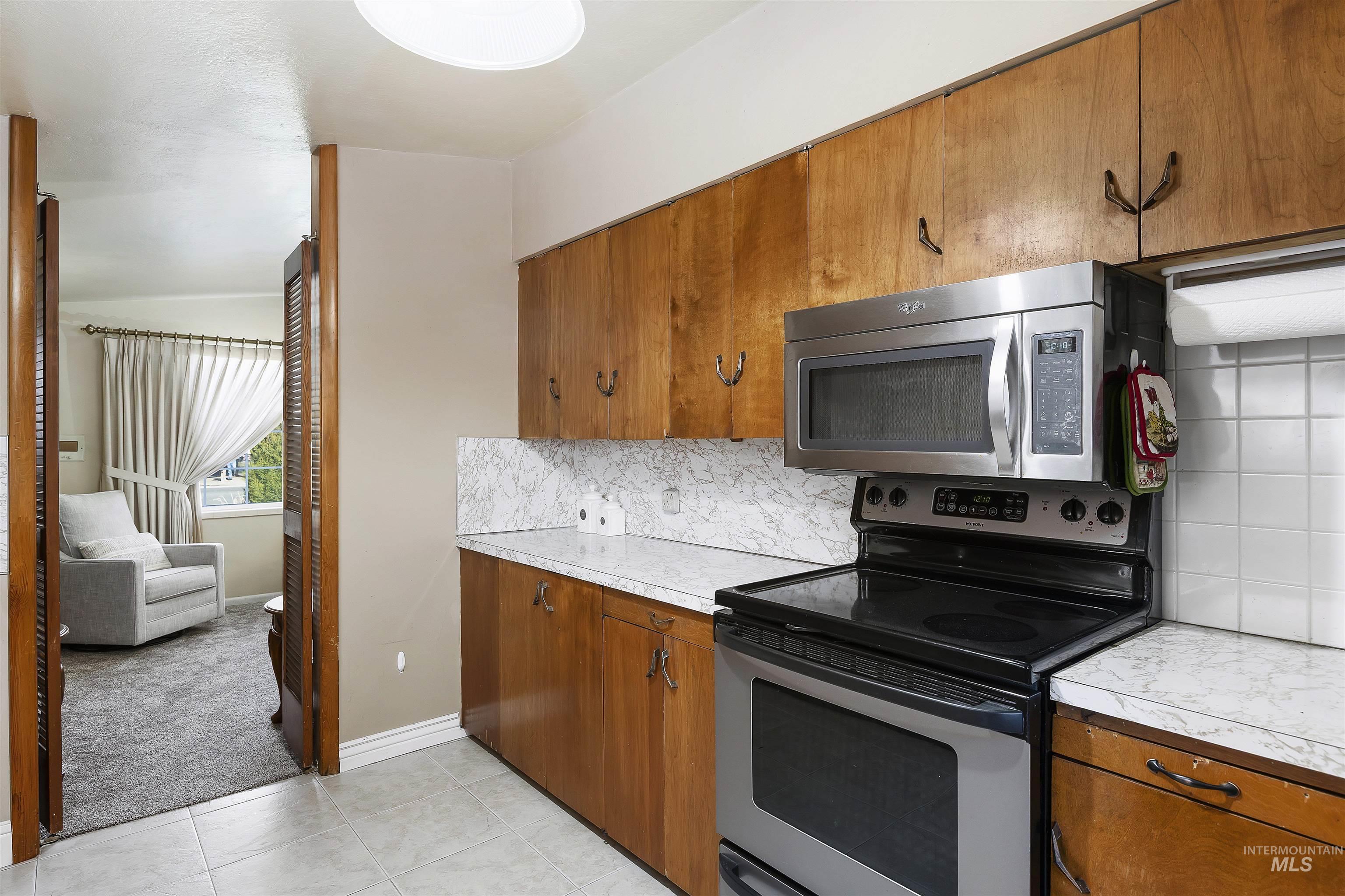 Kitchen featuring stainless steel appliances, decorative backsplash, brown cabinets, light countertops, and lofted ceiling