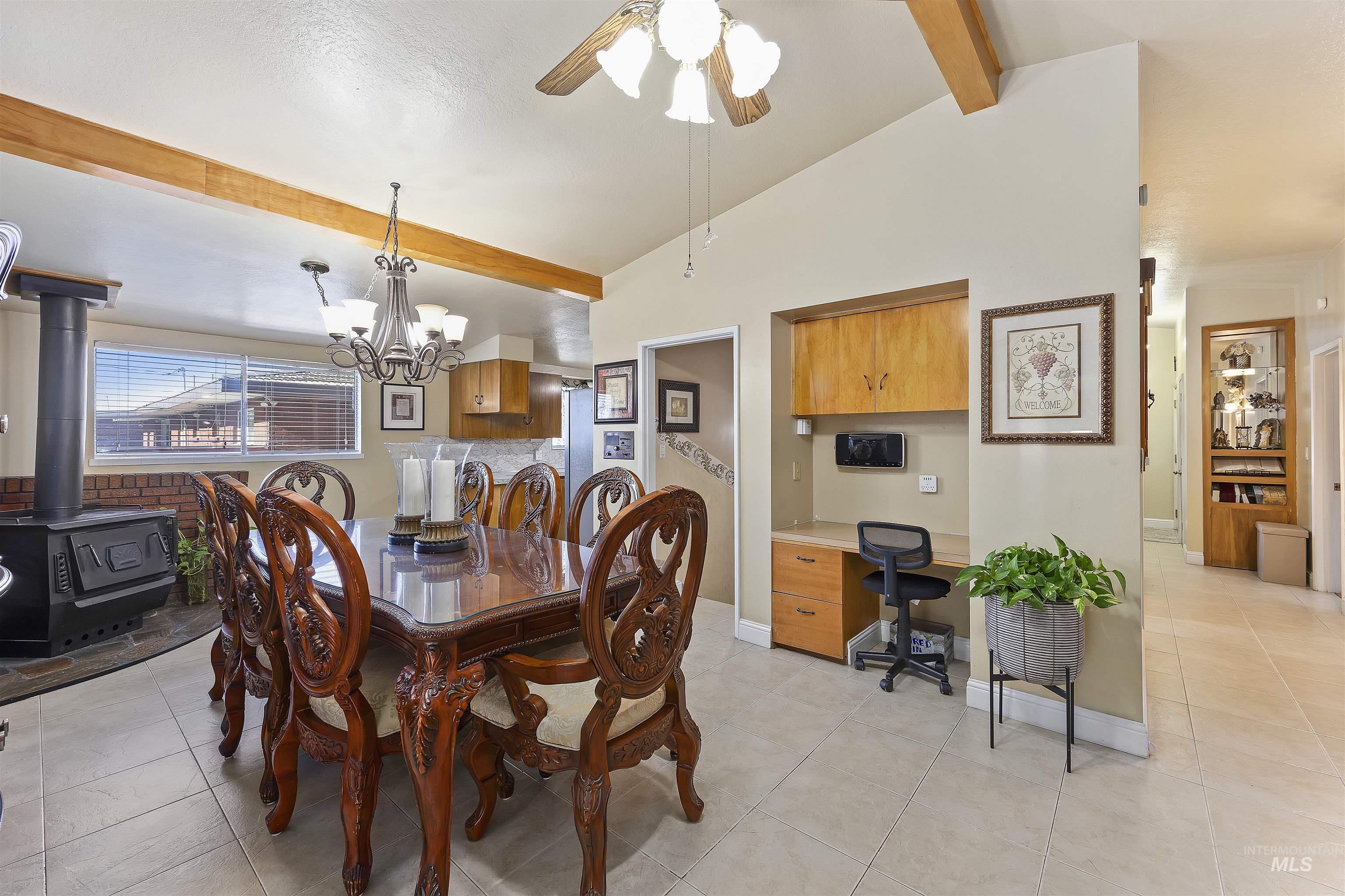 Dining room with light tile patterned flooring, a wood stove, a ceiling fan, an office area, and a chandelier