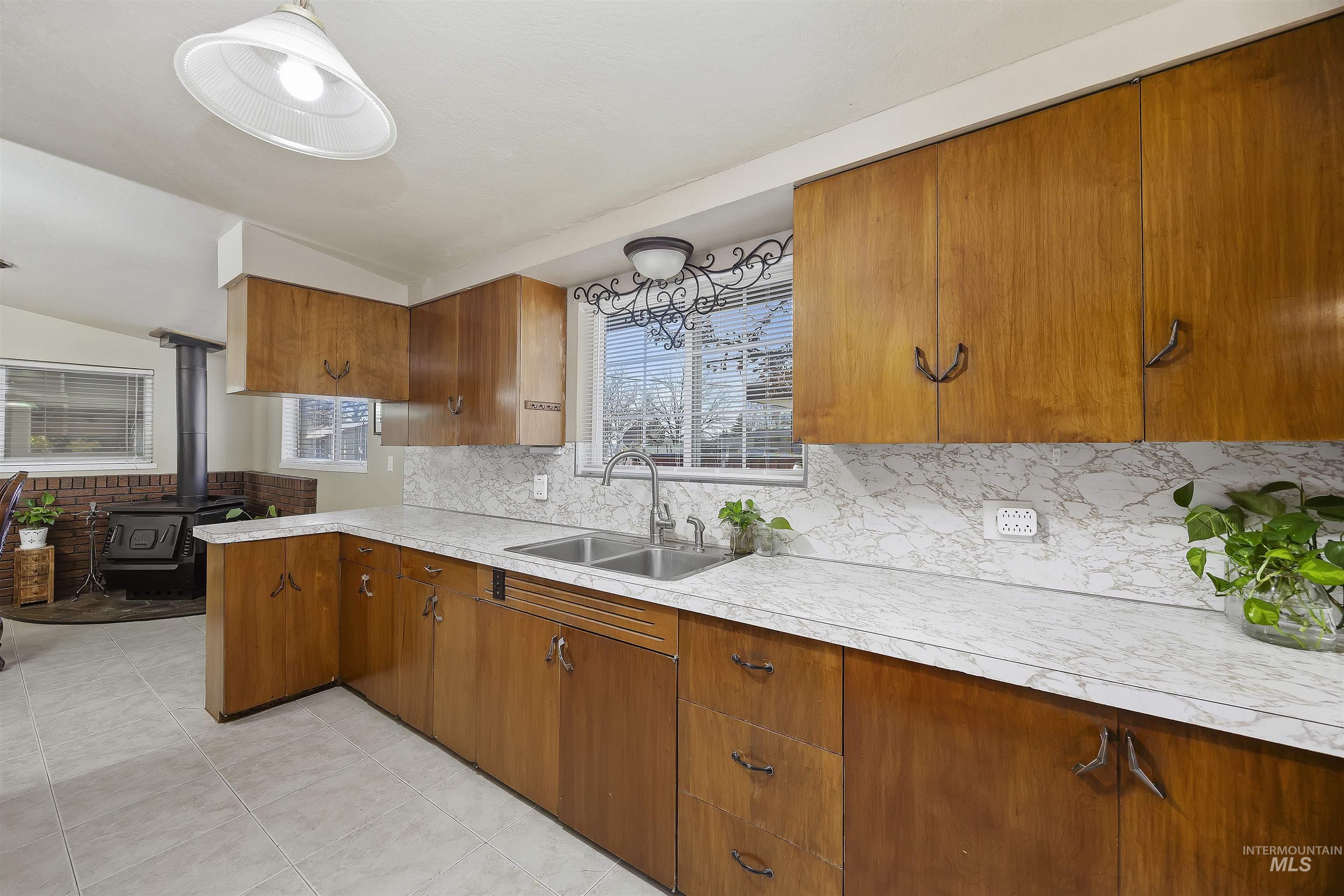 Kitchen featuring brown cabinets, vaulted ceiling, light countertops, backsplash, and a peninsula