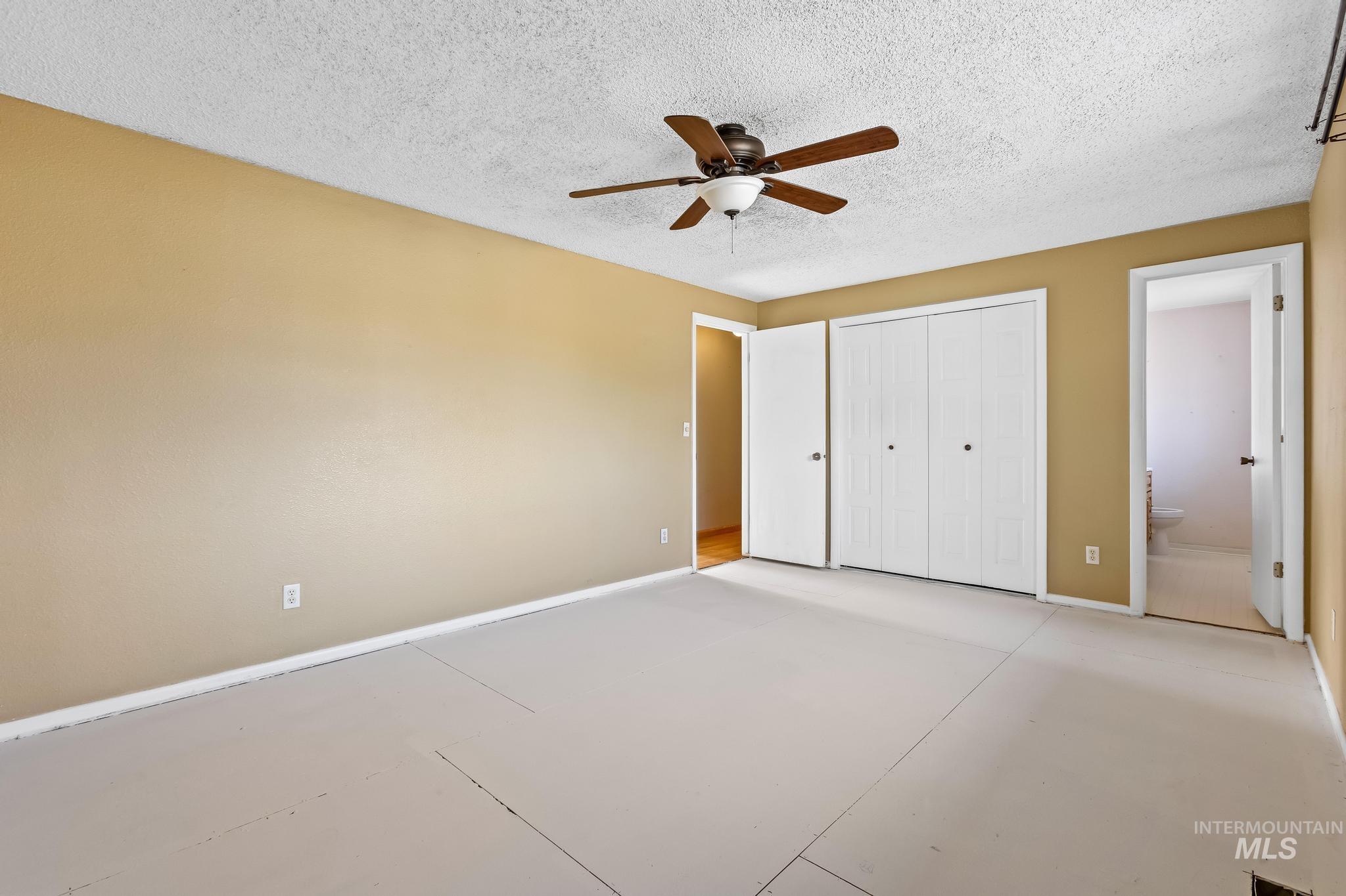 Unfurnished bedroom featuring a closet, a textured ceiling, a ceiling fan, and ensuite bathroom