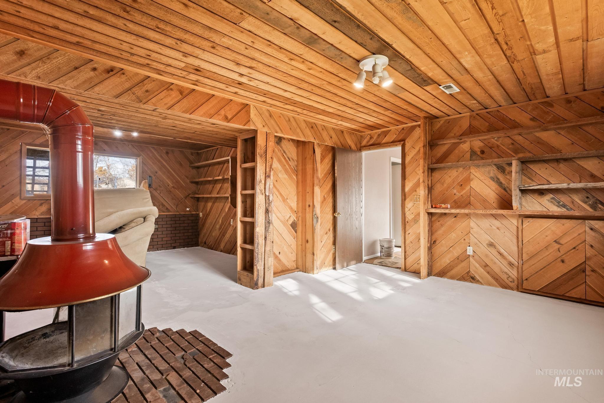 Miscellaneous room featuring wooden ceiling, wood walls, concrete floors, and a wood stove