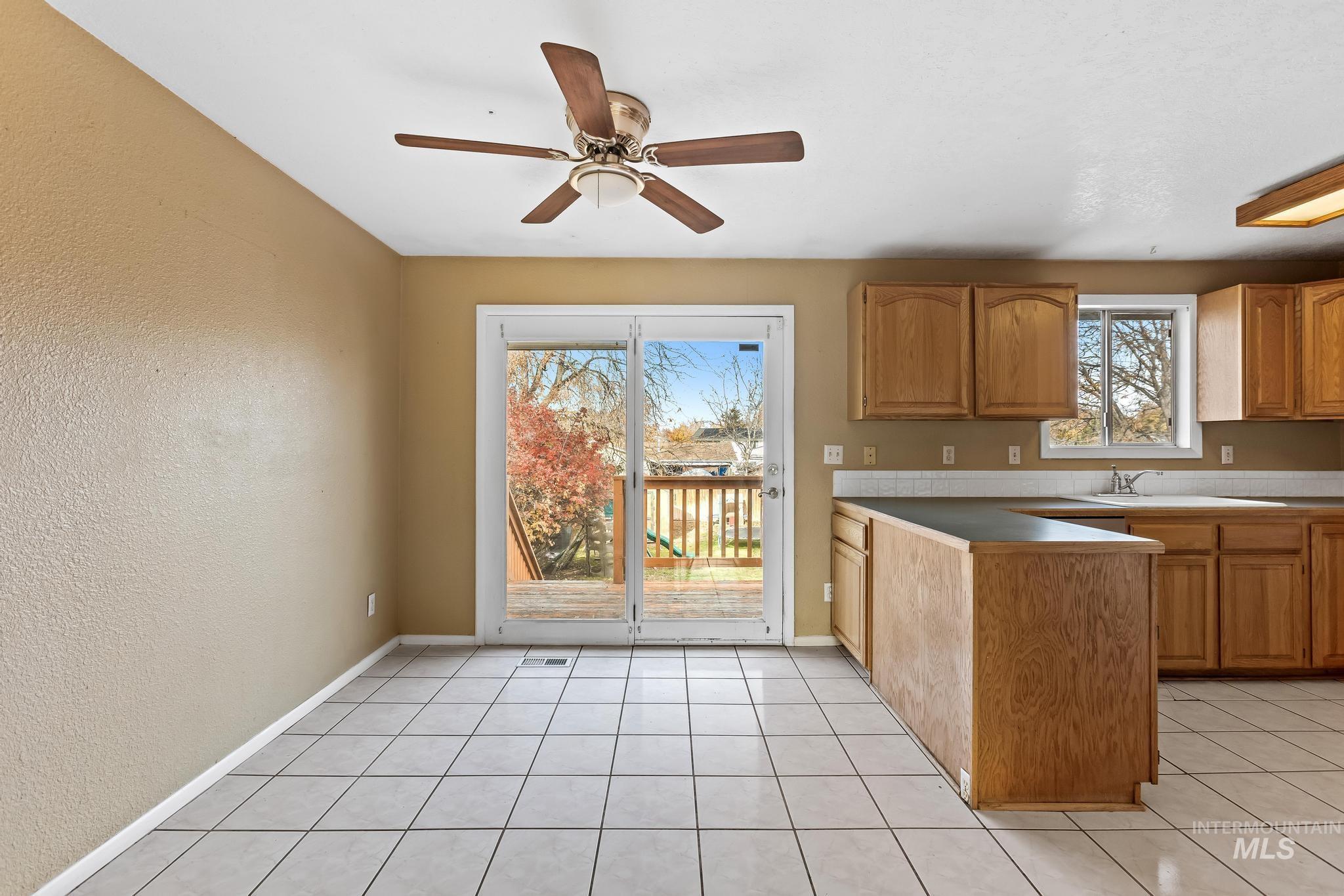Kitchen featuring a textured wall, brown cabinetry, light tile patterned floors, a peninsula, and ceiling fan