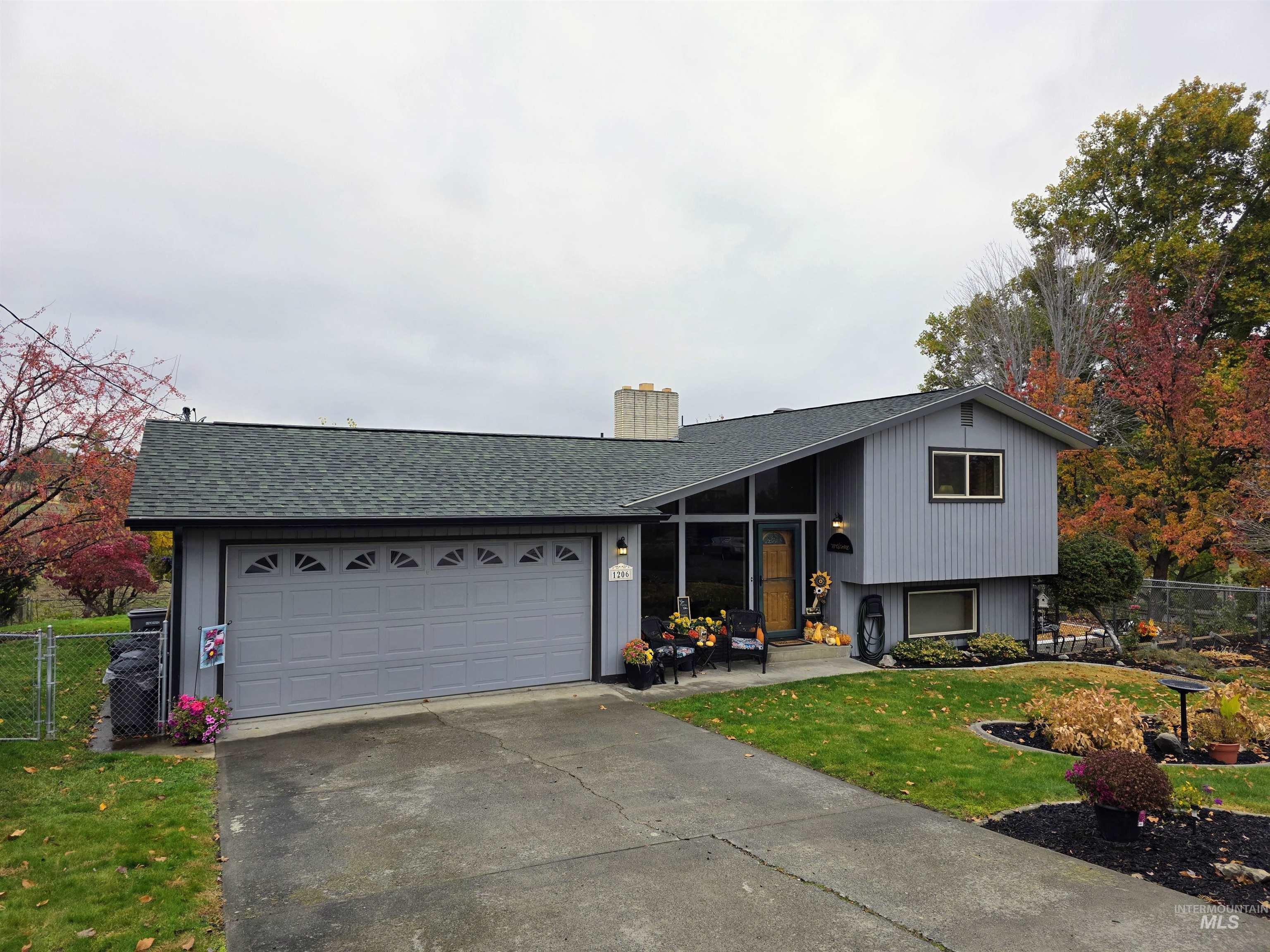 Tri-level home with a chimney, concrete driveway, a shingled roof, an attached garage, and a gate