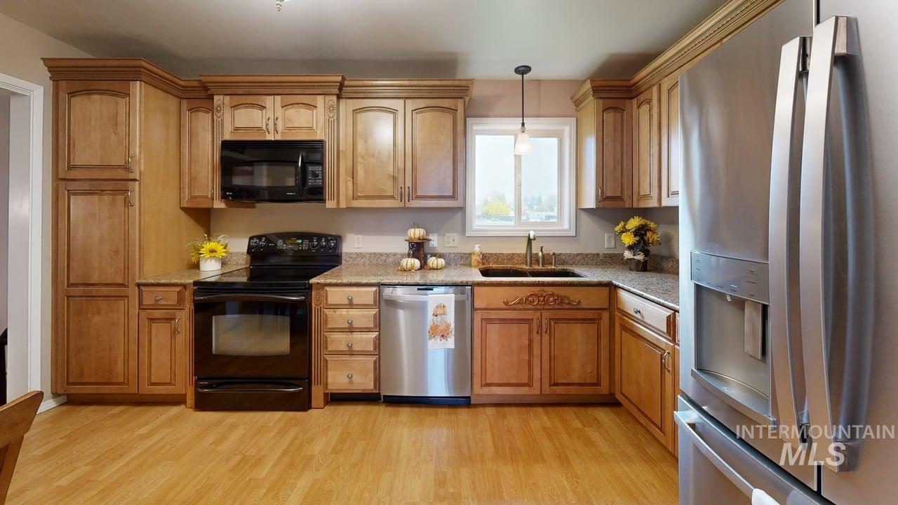 Kitchen with black appliances, light wood-style floors, light stone counters, and decorative light fixtures