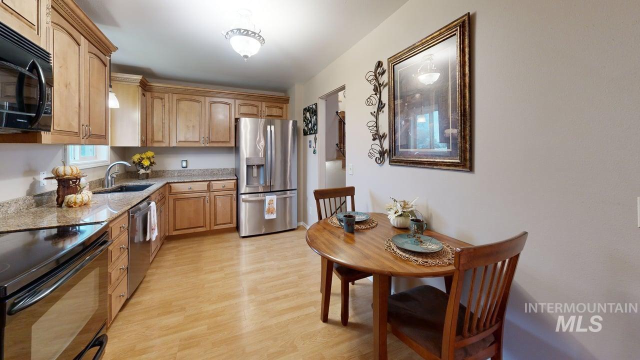Kitchen featuring black appliances, light wood-style floors, and light stone countertops