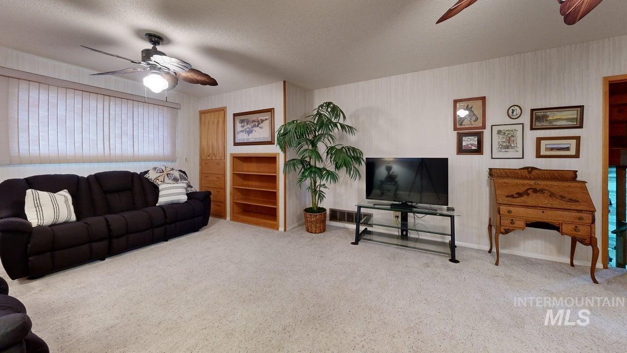Living room with a ceiling fan, light colored carpet, and a textured ceiling