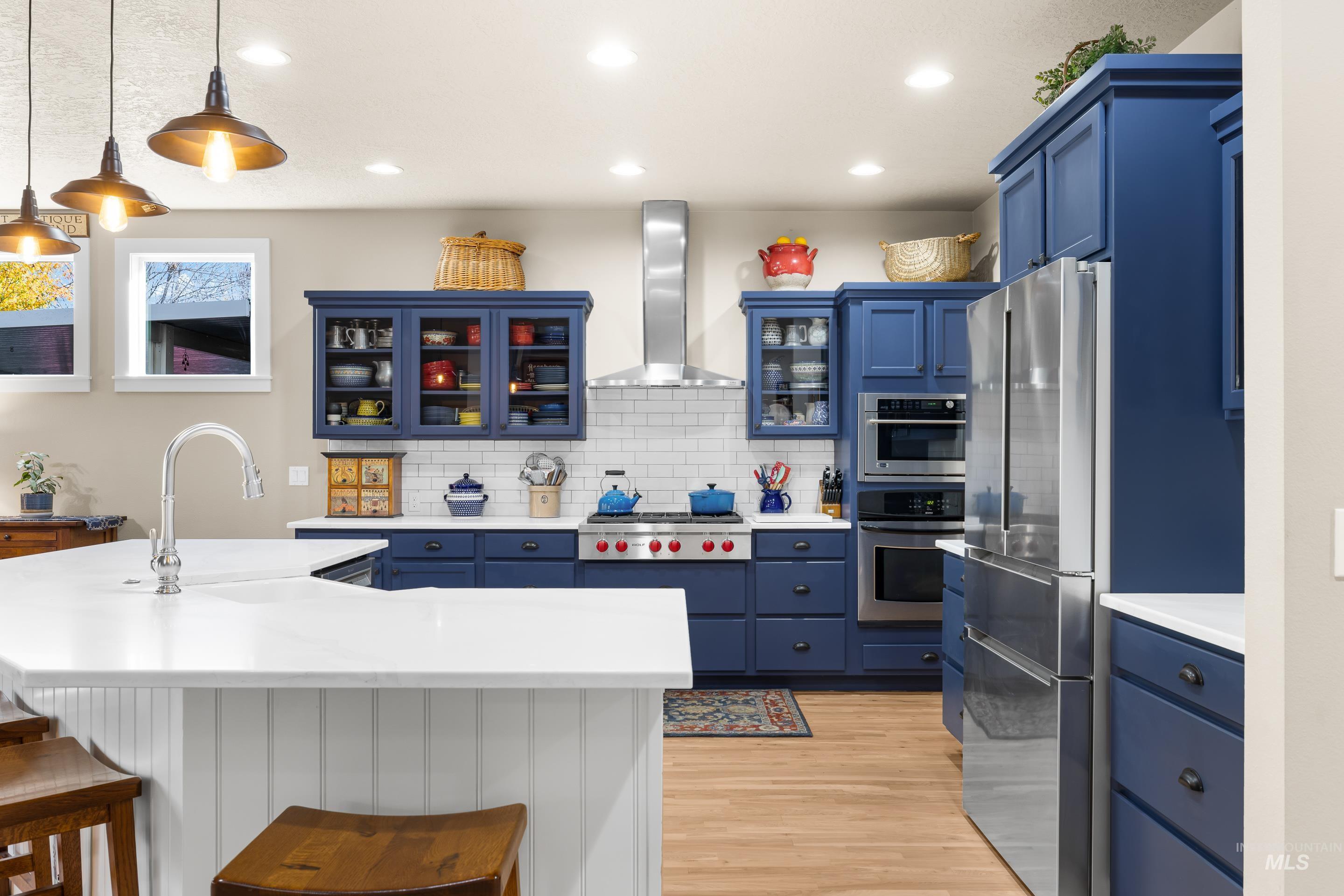Kitchen featuring blue cabinetry, glass insert cabinets, decorative backsplash, an island with sink, and decorative light fixtures