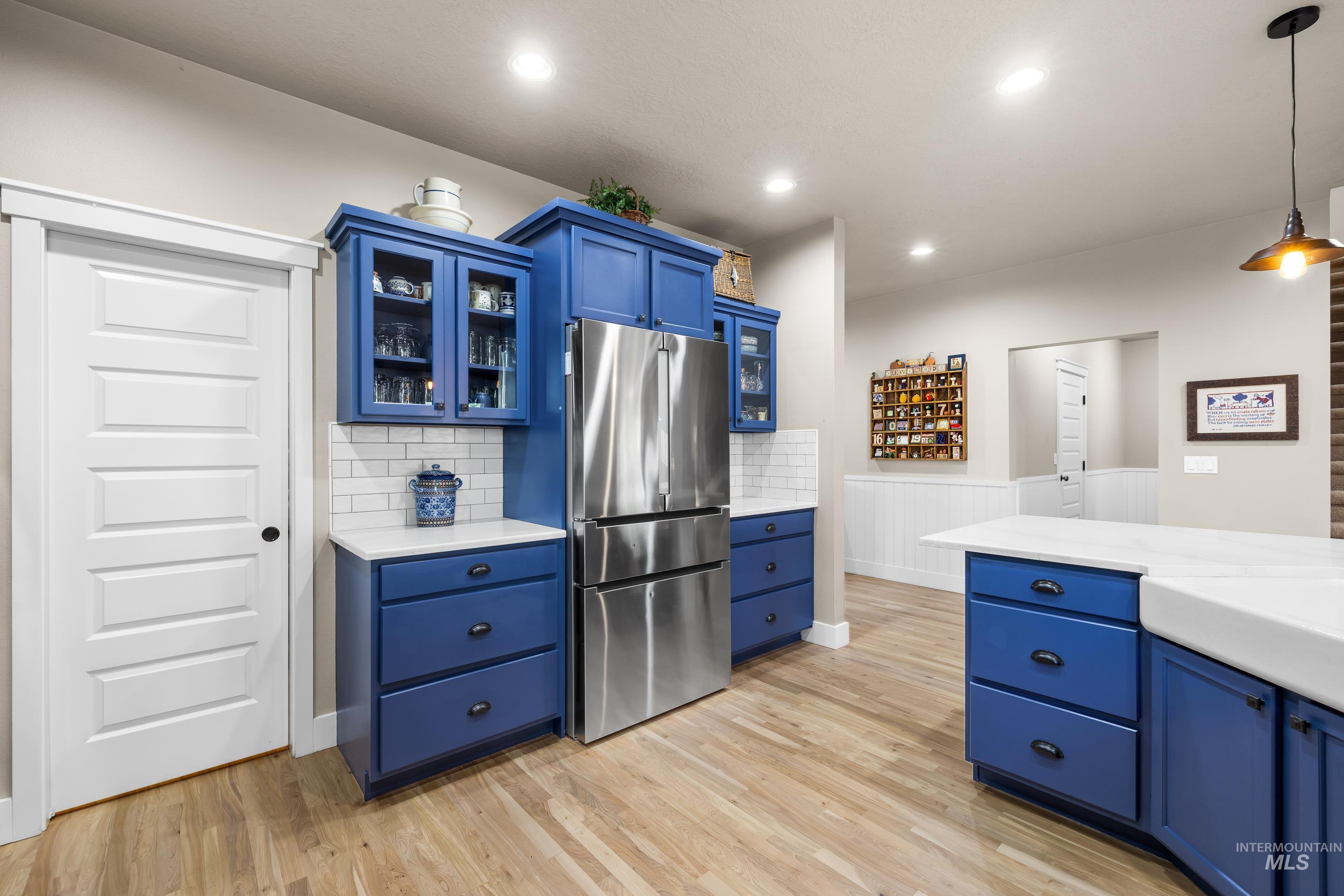 Kitchen featuring blue cabinets, glass insert cabinets, freestanding refrigerator, hanging light fixtures, and light wood finished floors
