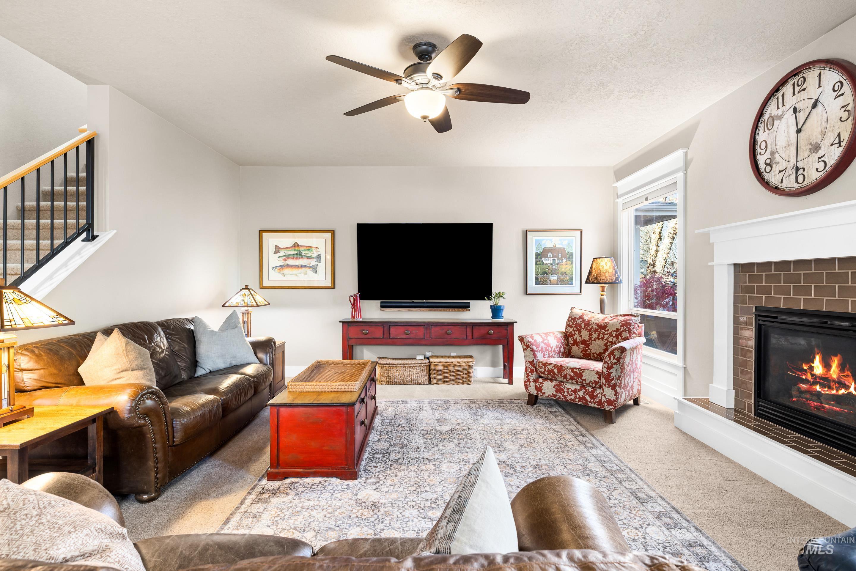 Living area with carpet flooring, stairs, a ceiling fan, and a glass covered fireplace