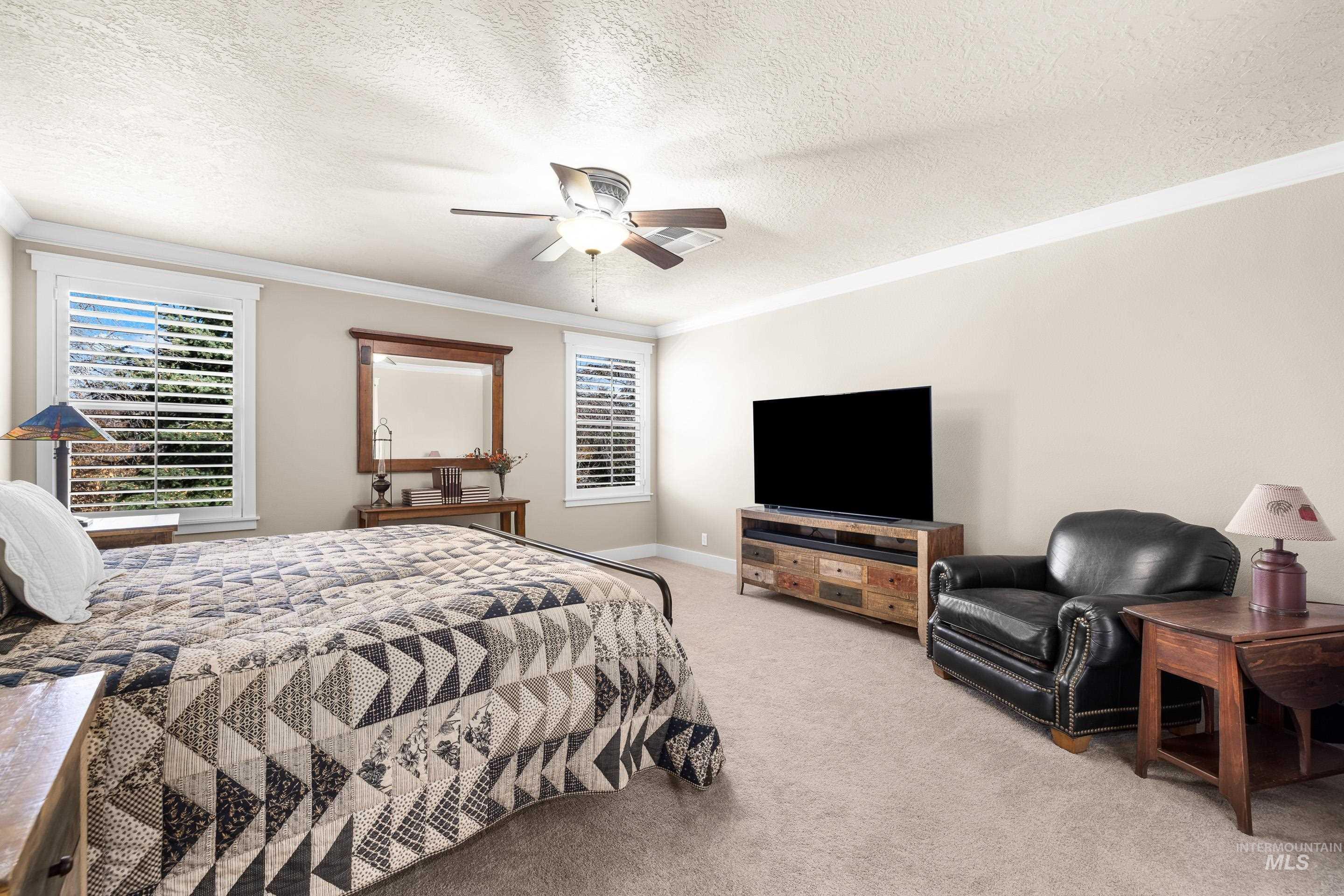 Bedroom featuring a textured ceiling, light colored carpet, crown molding, and ceiling fan