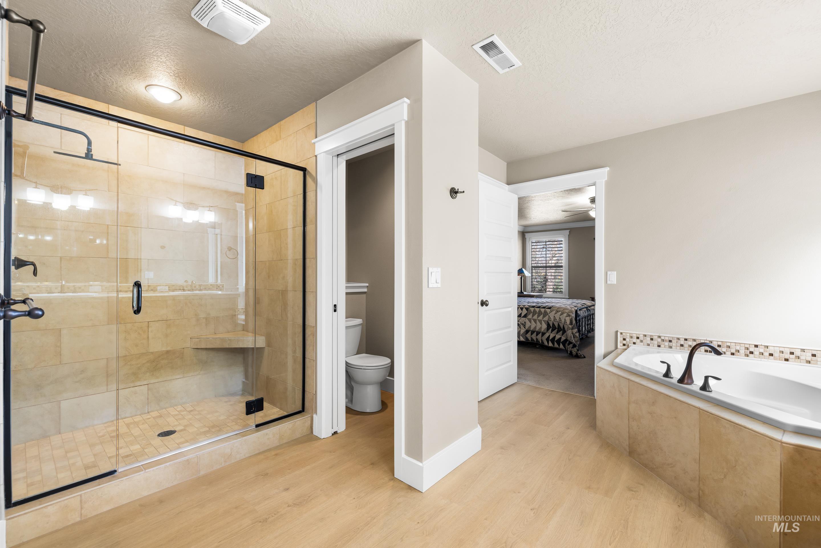 Bathroom with a textured ceiling, ensuite bath, light wood-type flooring, a garden tub, and a stall shower