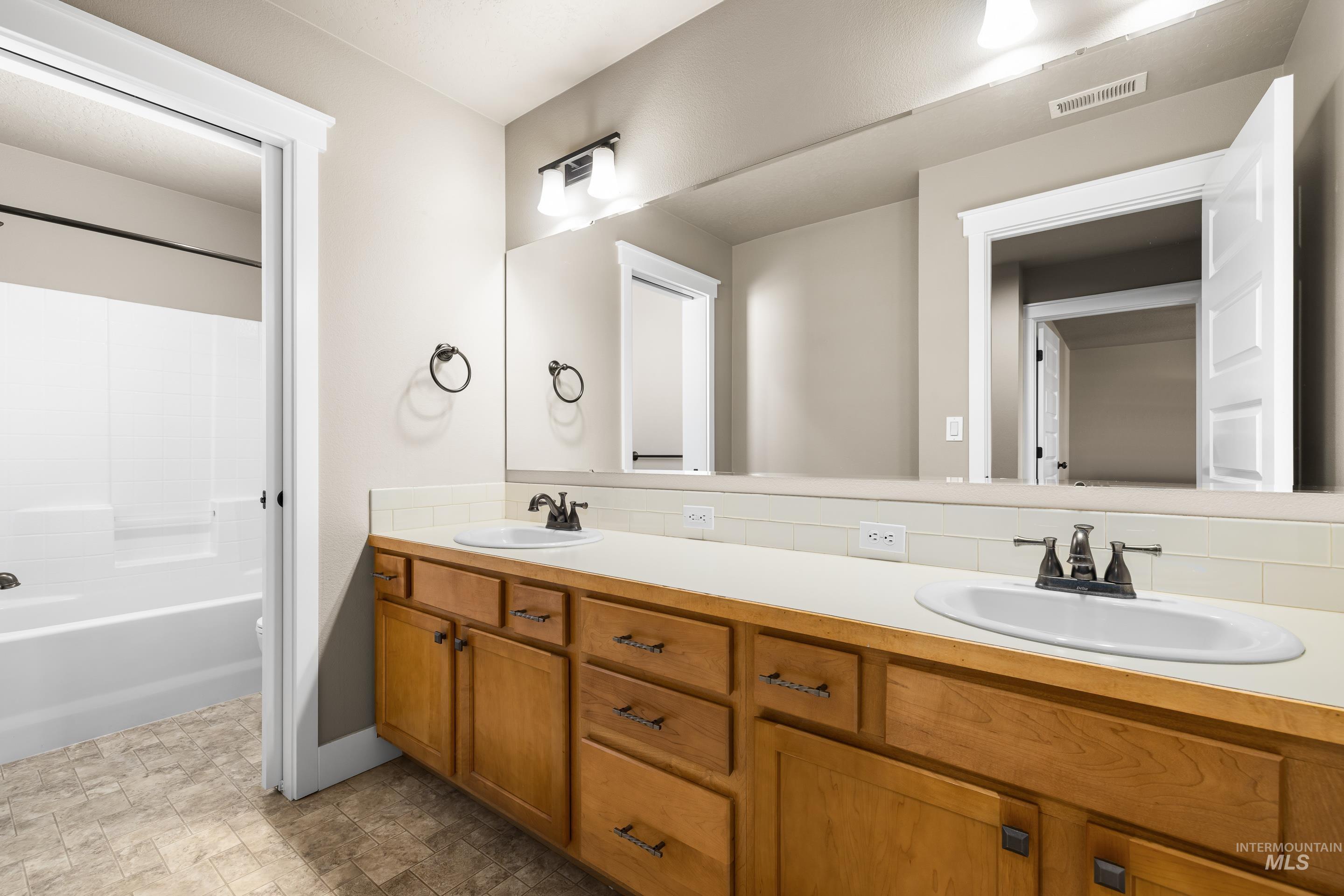 Bathroom featuring double vanity, shower / tub combination, and stone finish flooring