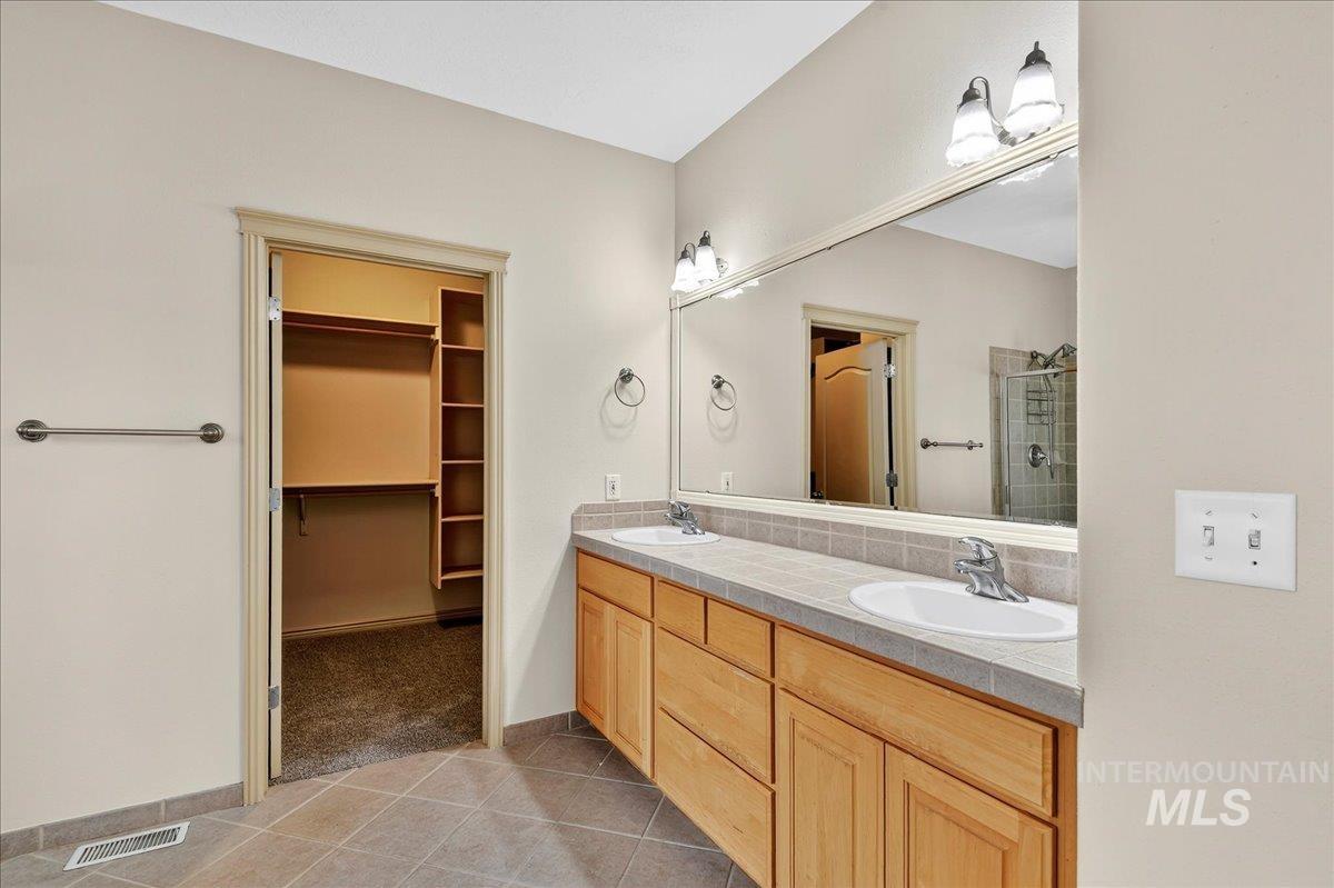 Bathroom with light tile patterned flooring, double vanity, a spacious closet, a stall shower, and light colored carpet