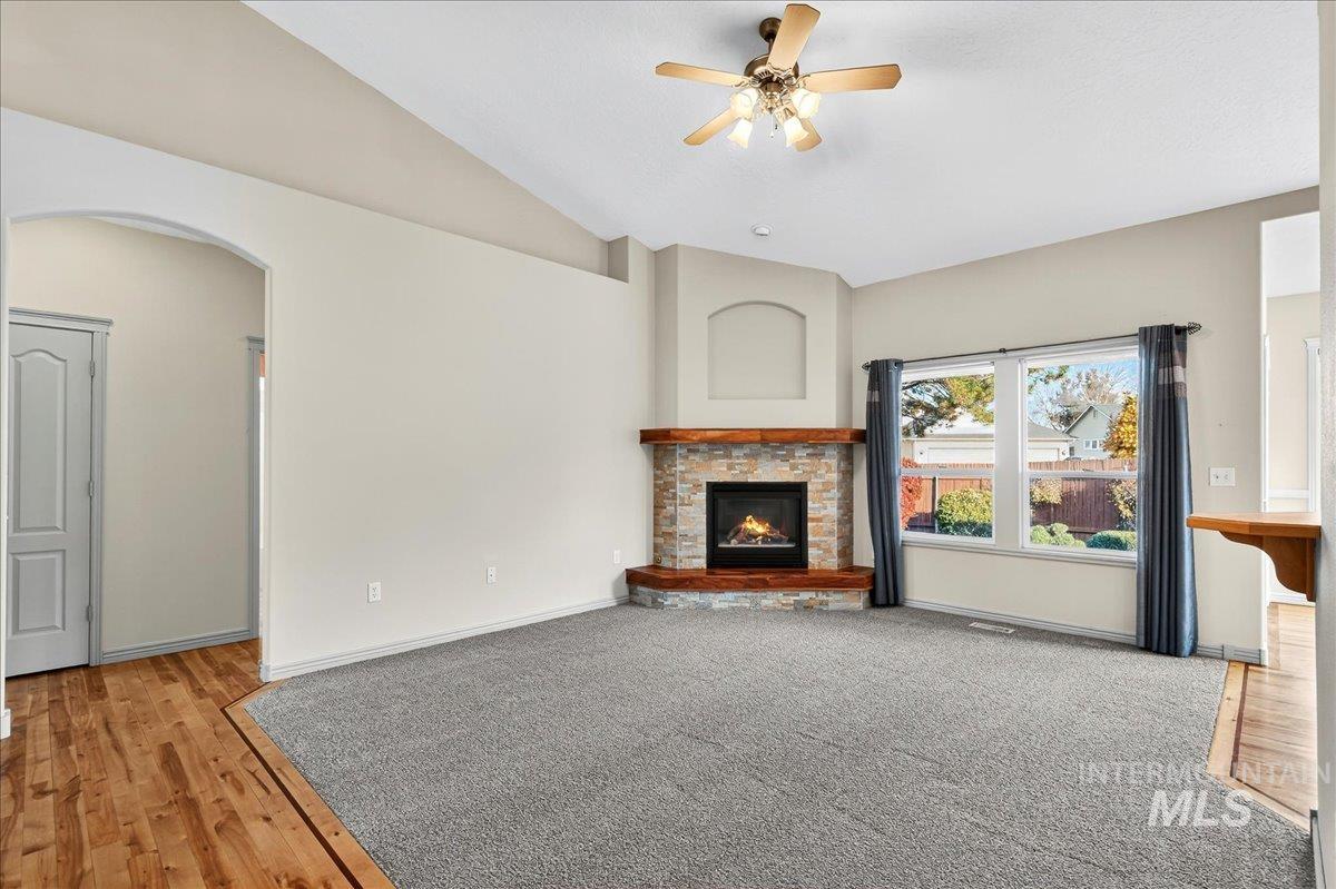 Unfurnished living room with vaulted ceiling, light wood-style flooring, a fireplace, arched walkways, and a ceiling fan