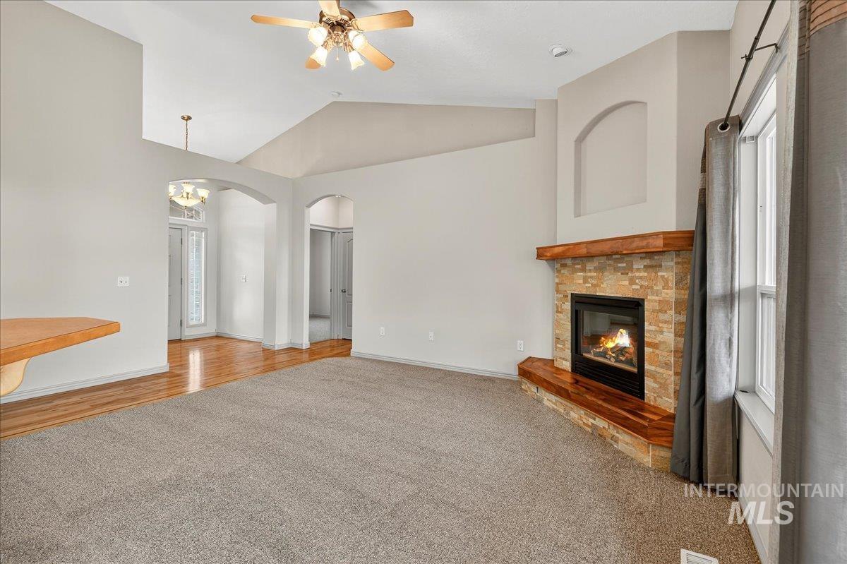 Unfurnished living room with vaulted ceiling, carpet, a glass covered fireplace, arched walkways, and ceiling fan