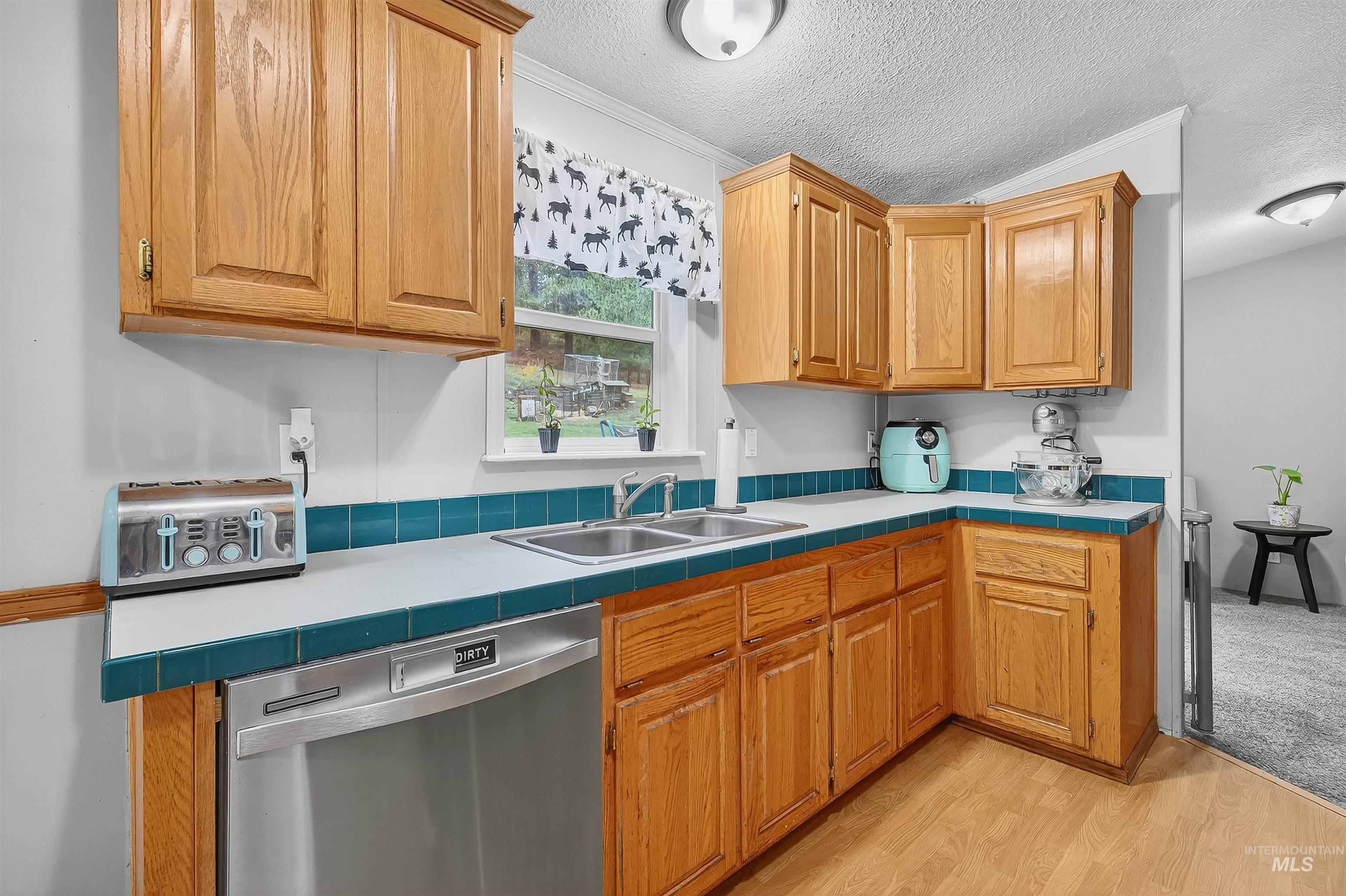Kitchen with tile counters, dishwasher, a textured ceiling, light wood finished floors, and crown molding