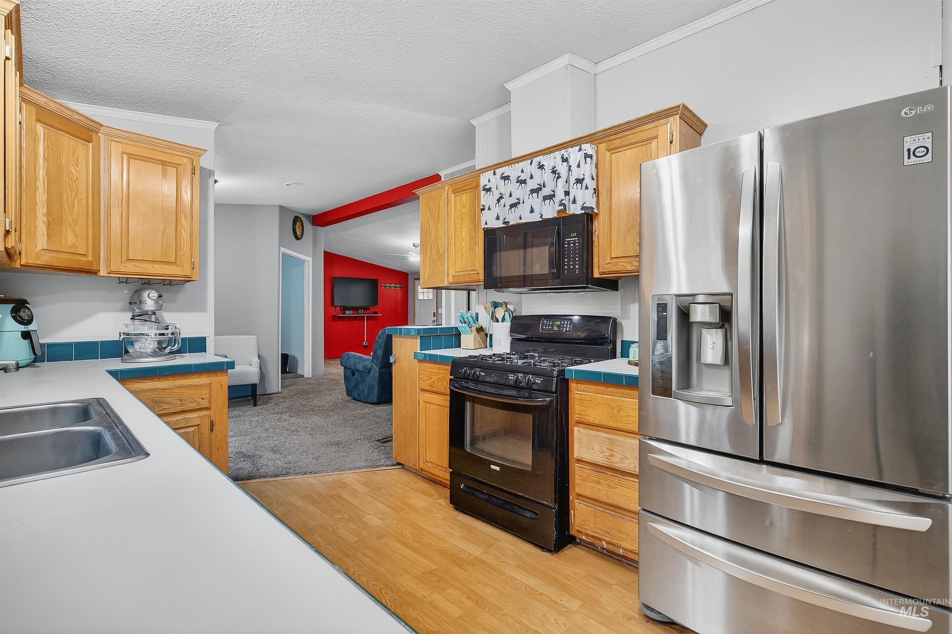 Kitchen with black appliances, light wood-type flooring, a textured ceiling, ornamental molding, and tile counters