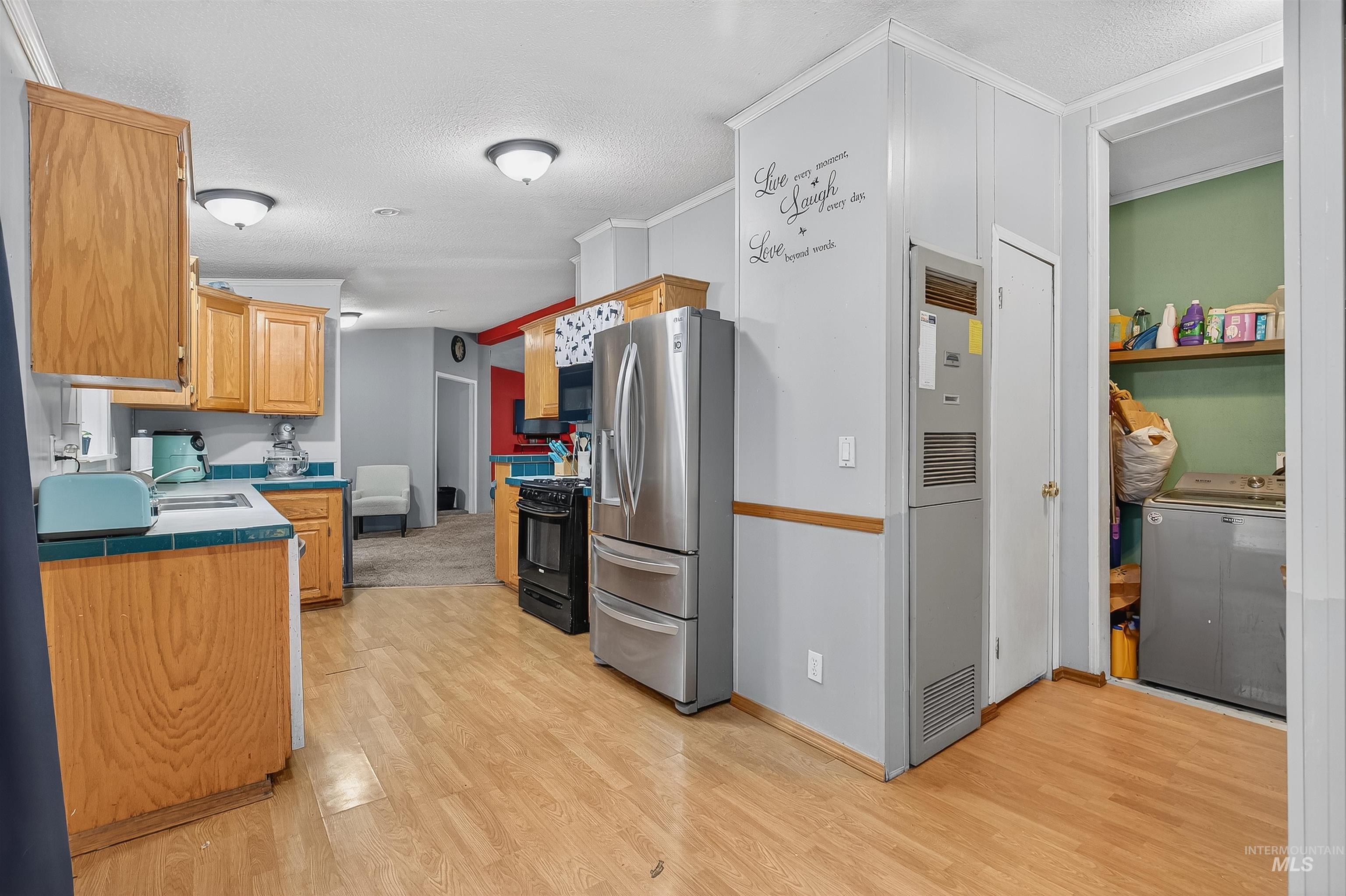 Kitchen featuring tile counters, light wood finished floors, stainless steel fridge with ice dispenser, a heating unit, and a textured ceiling