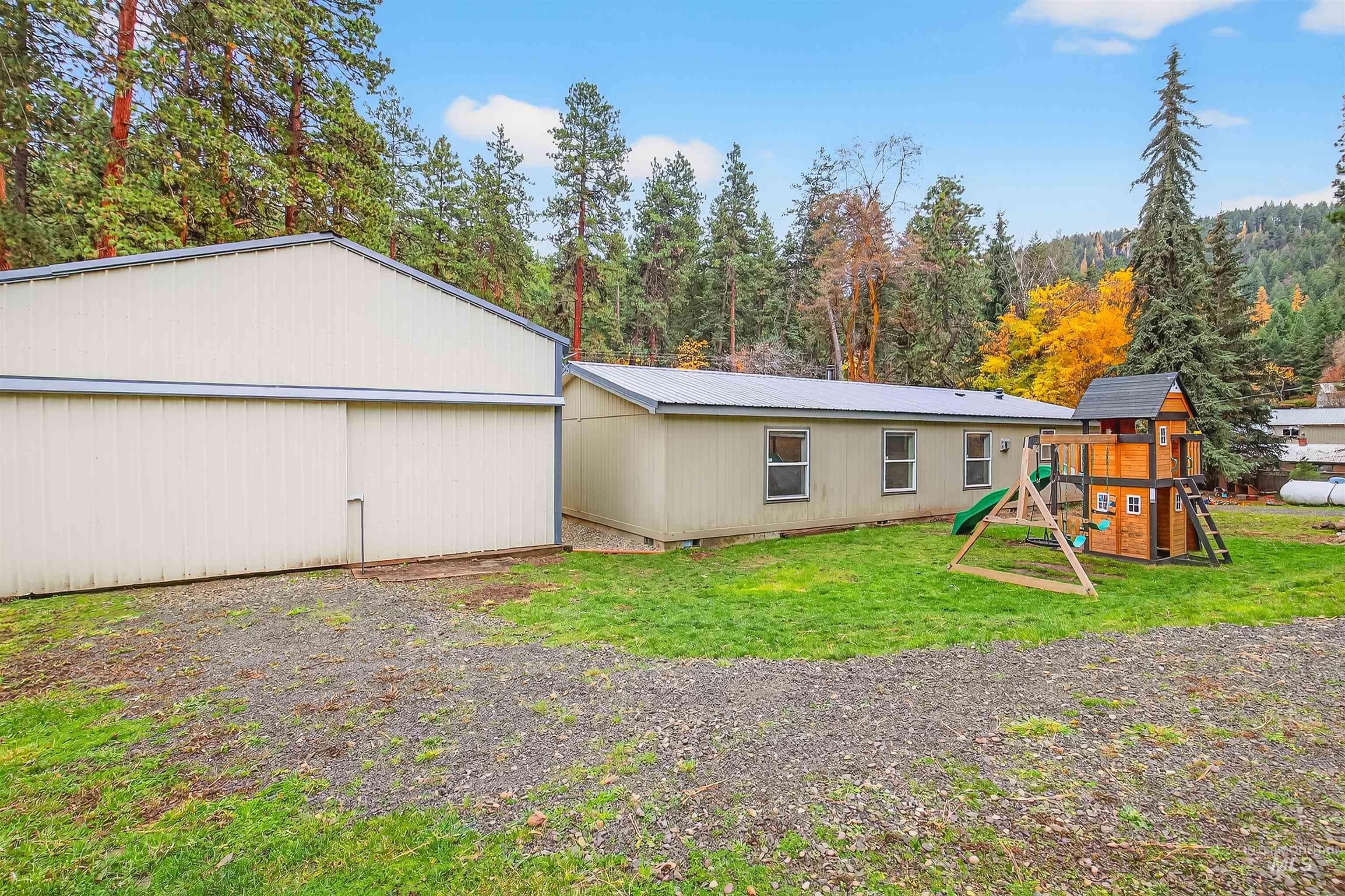 Back of house with a playground, a yard, a metal roof, and a view of trees