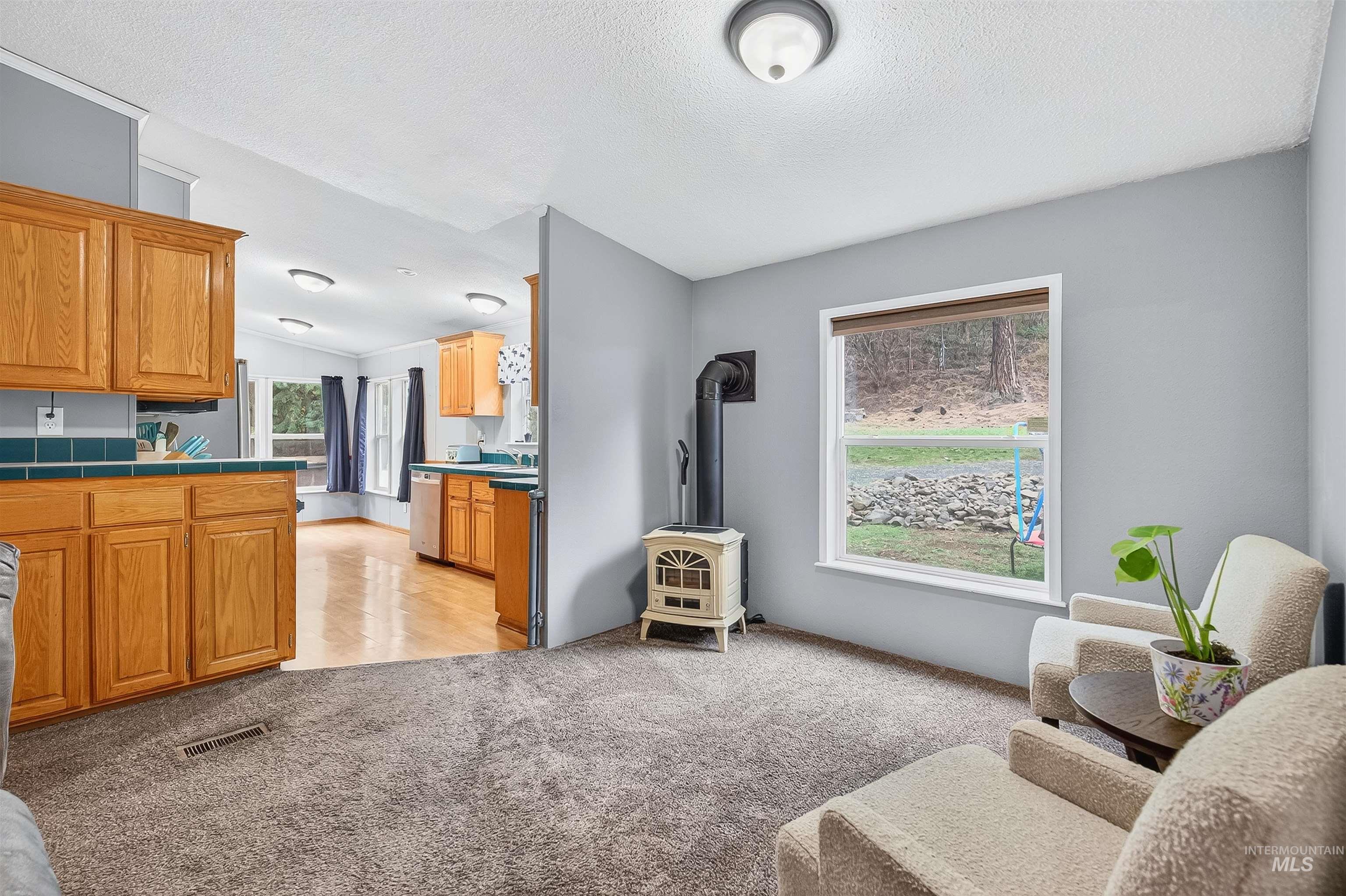 Living area with light colored carpet, a wood stove, a textured ceiling, and vaulted ceiling