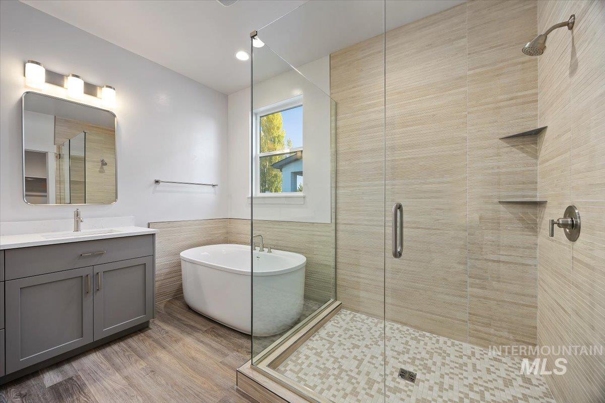Bathroom featuring tile walls, a freestanding bath, vanity, a shower stall, and light wood-style flooring